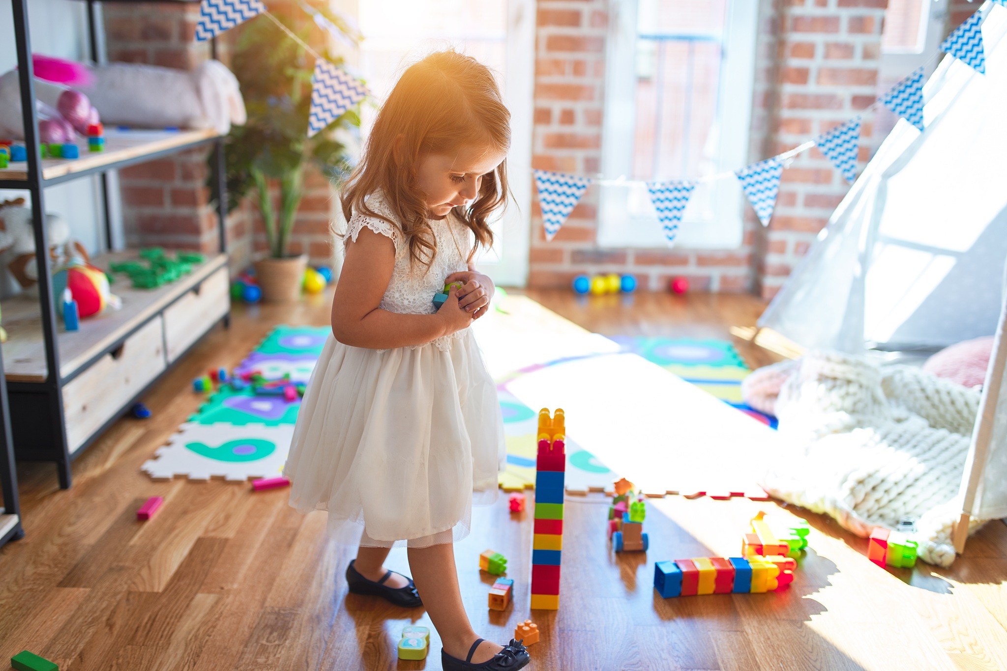 adorable blonde toddler playing around lots of toys at kindergar