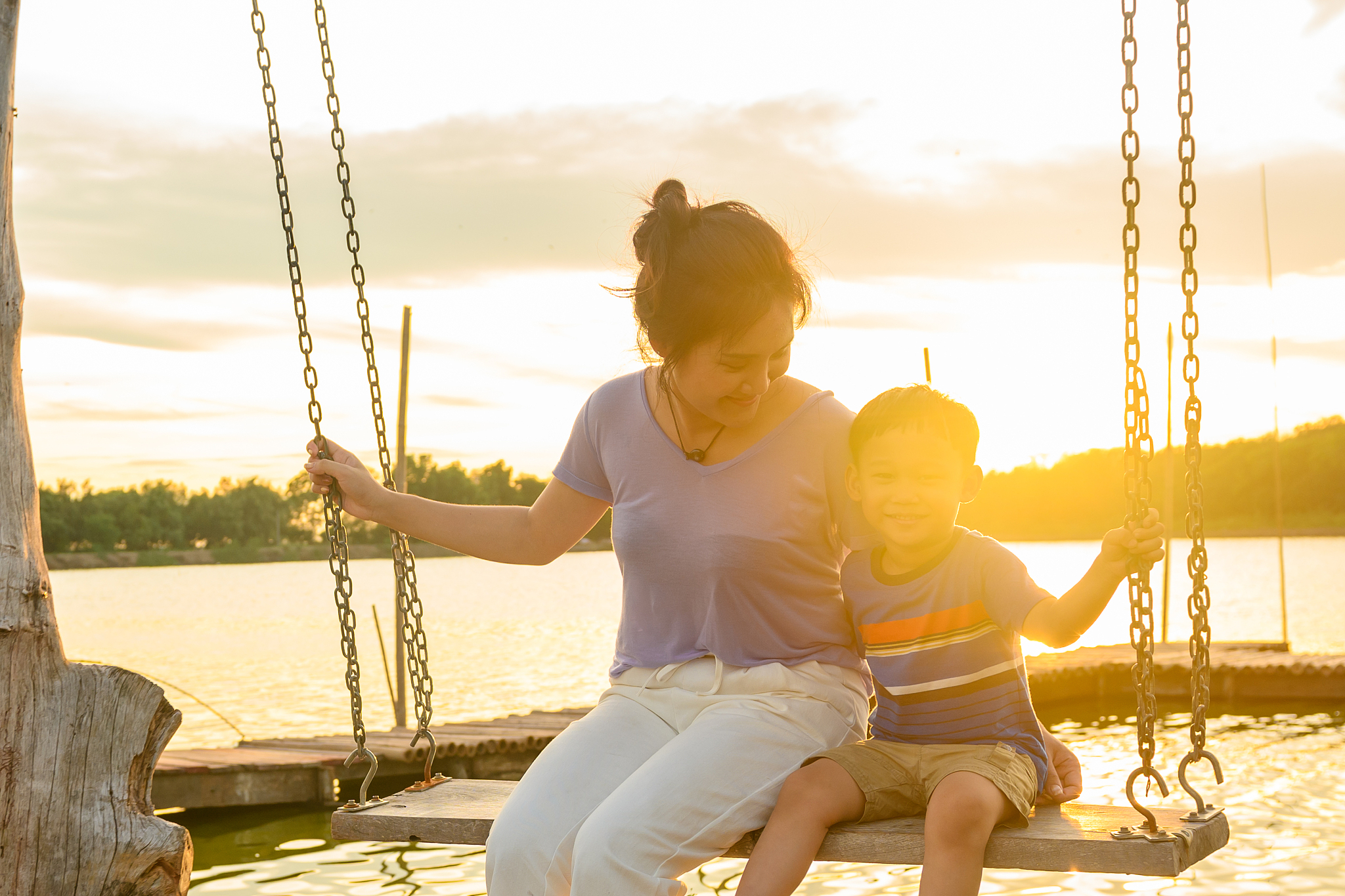 smiling mother sitting on swing with son during sunset