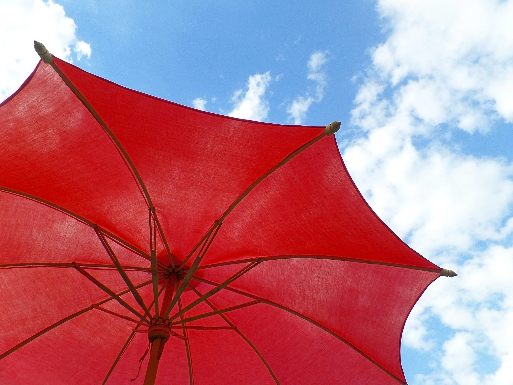 one red colored sunshade against vivid blue sky and fluffy white