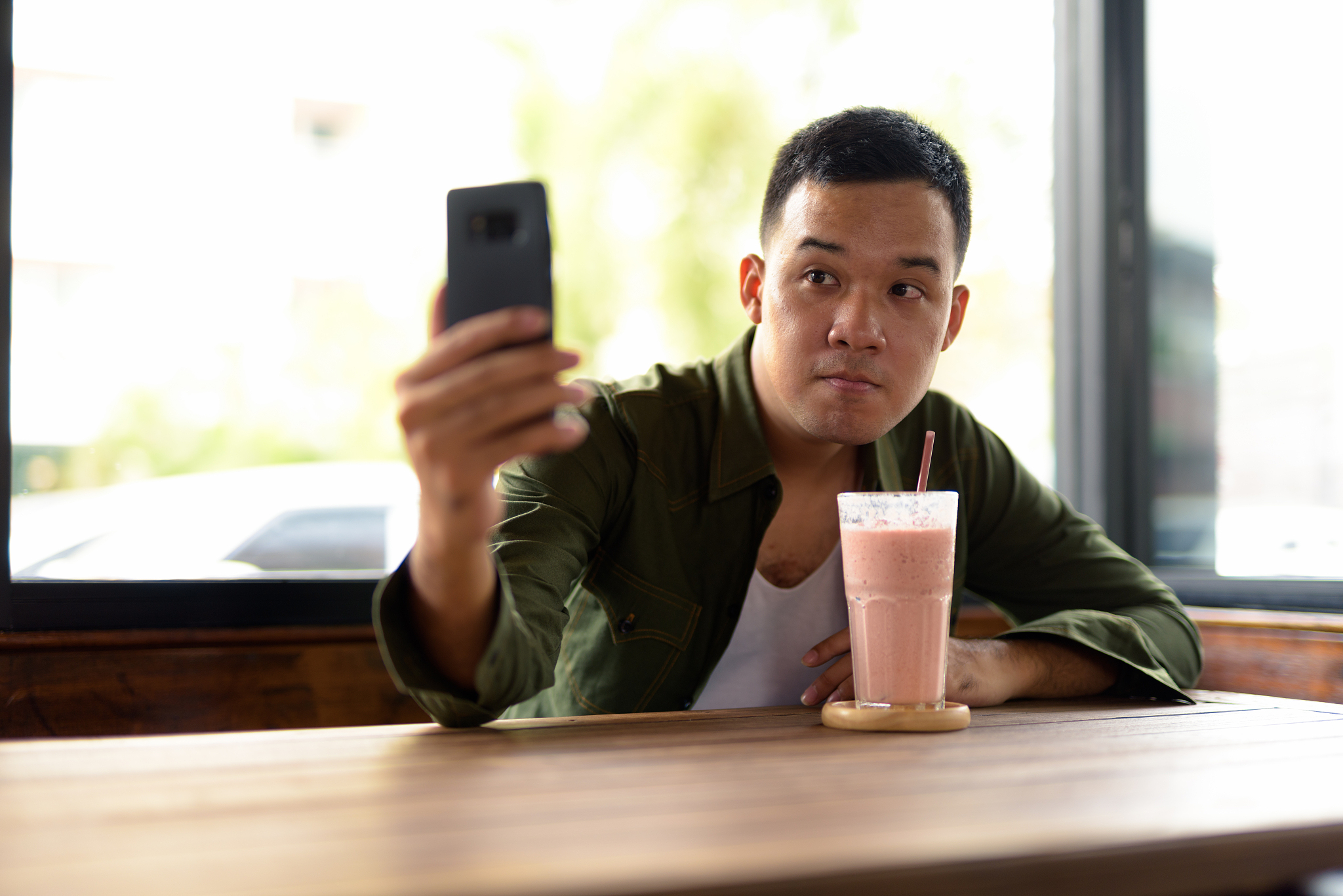 young asian man sitting in coffee shop and drinking strawberry m