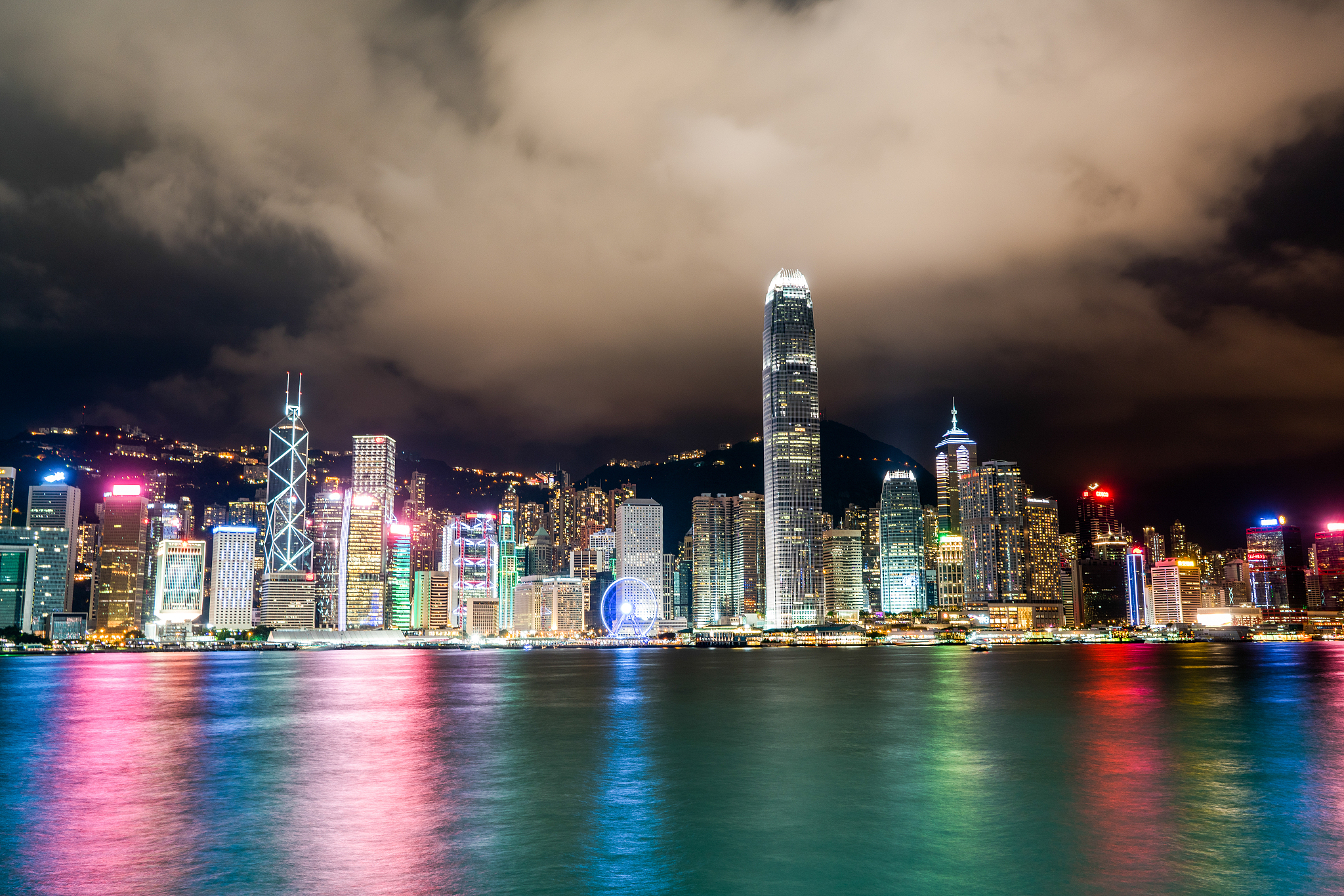 illuminated city at waterfront against cloudy sky