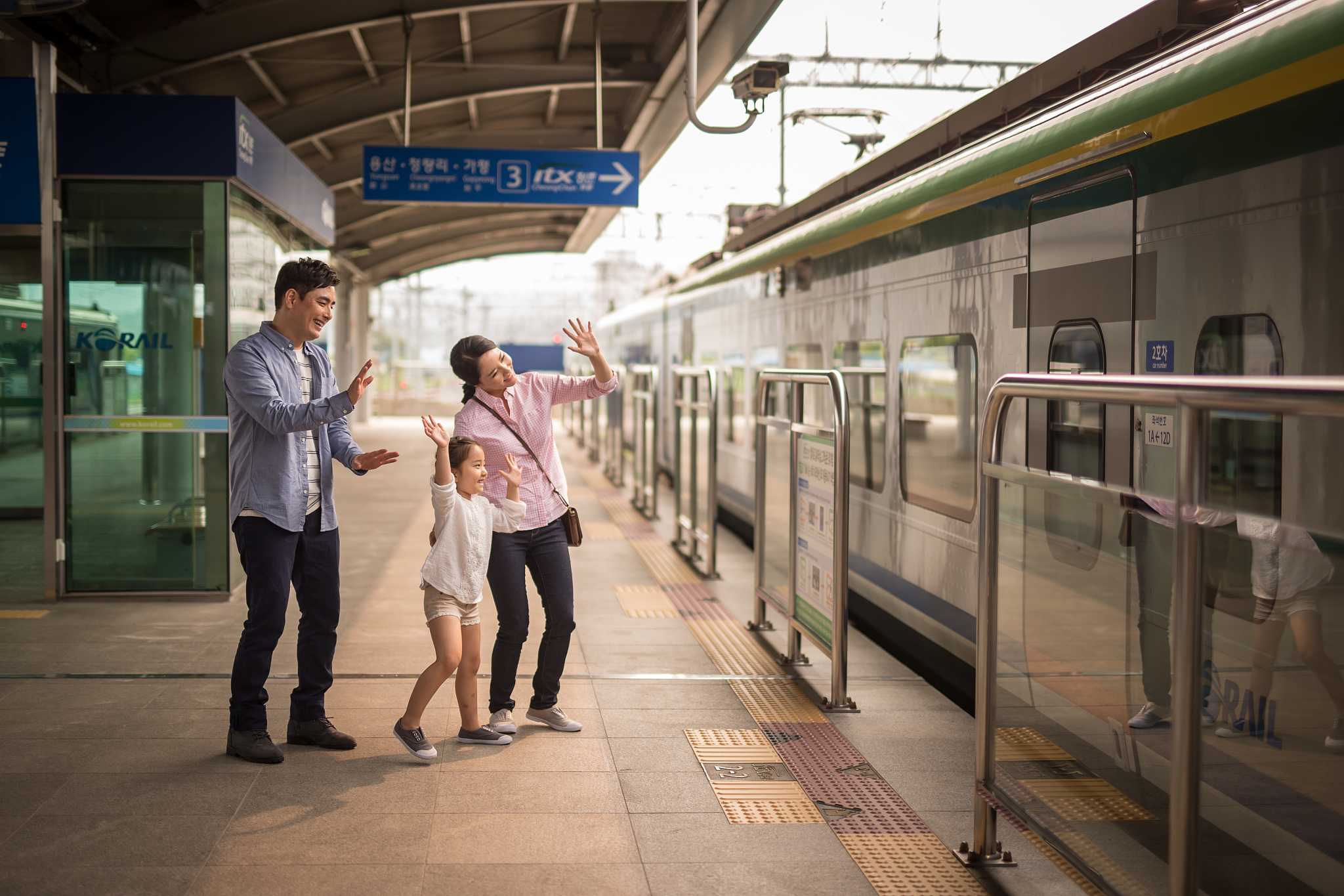 family with daughter waving hands at train station platform