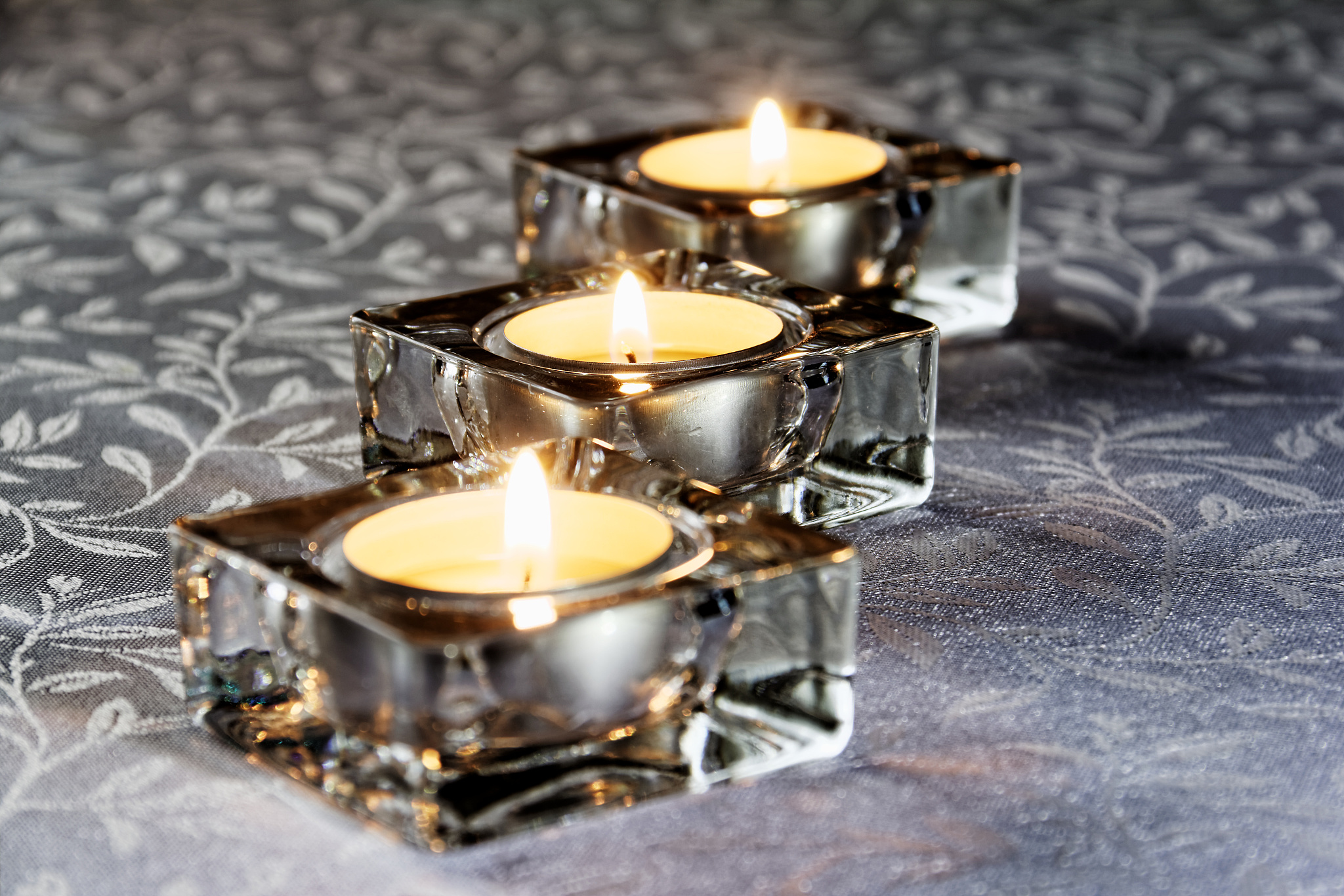 three lit candles in glass on a white tablecloth