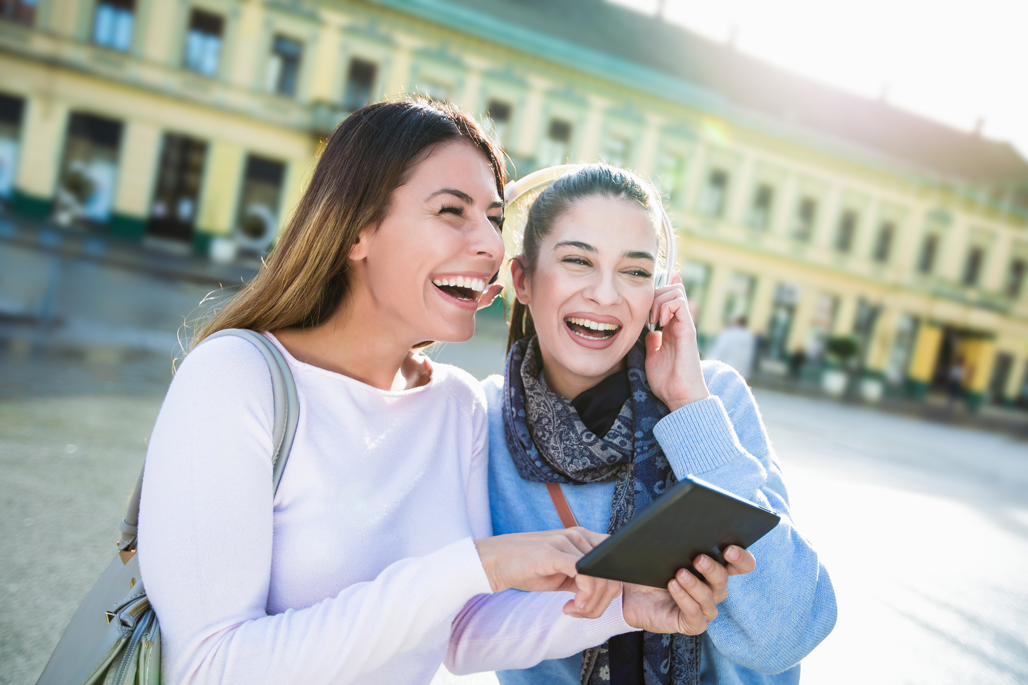 two girl friends laughing at tablet outdoors street