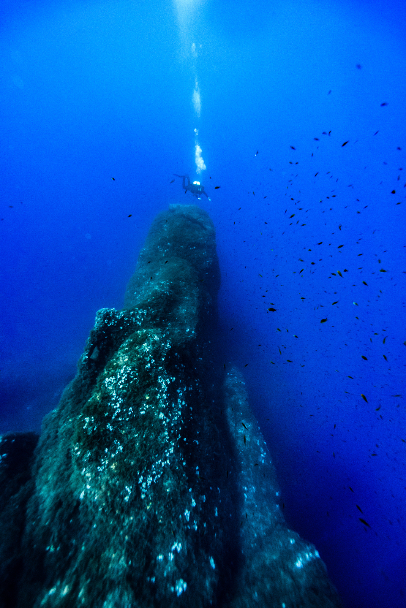 distant view of scuba diver swimming over rock formation in sea