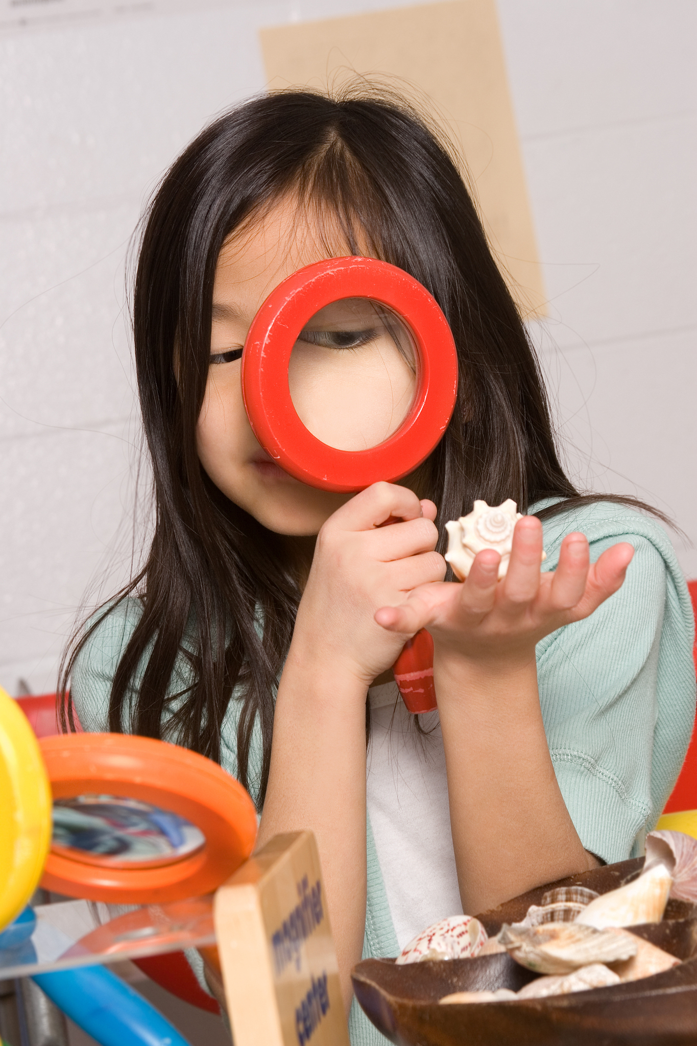 young girl looks at shell through magnifying glass