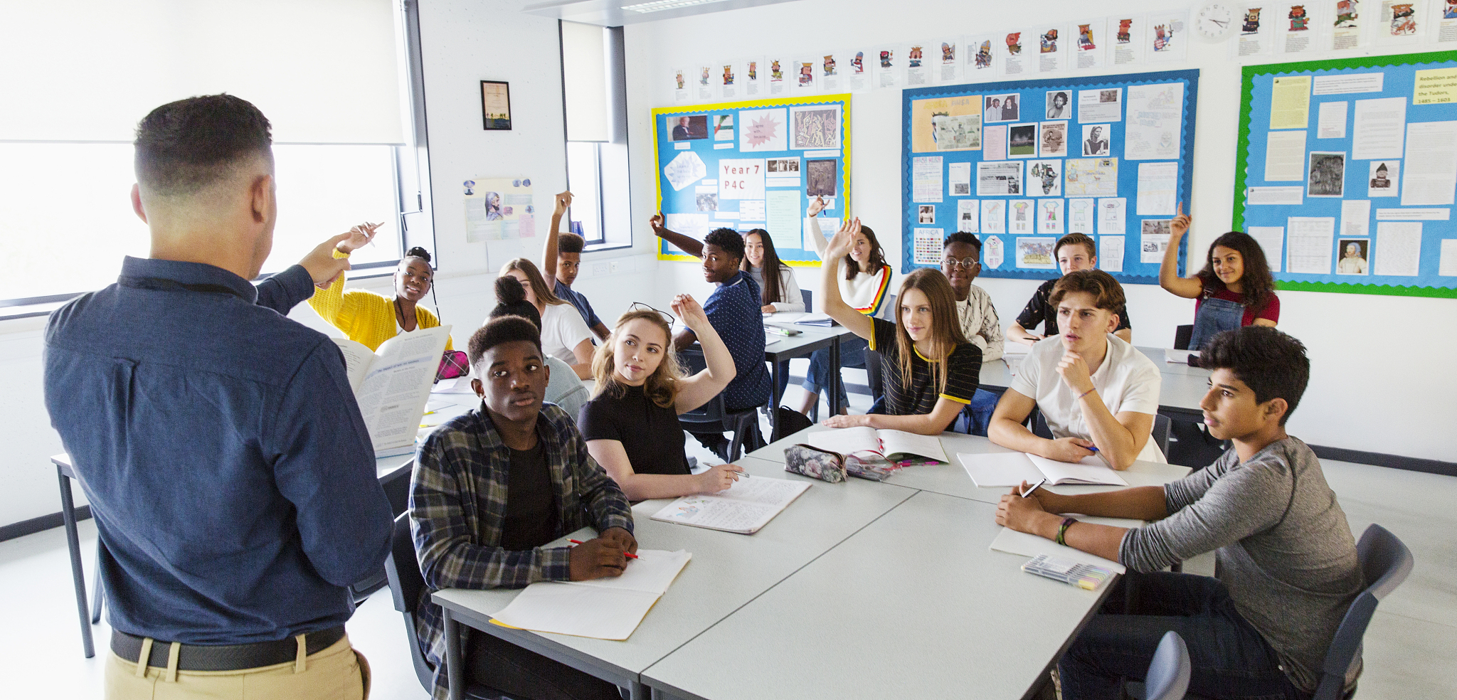 high school teacher calling on students with hands raised in cla