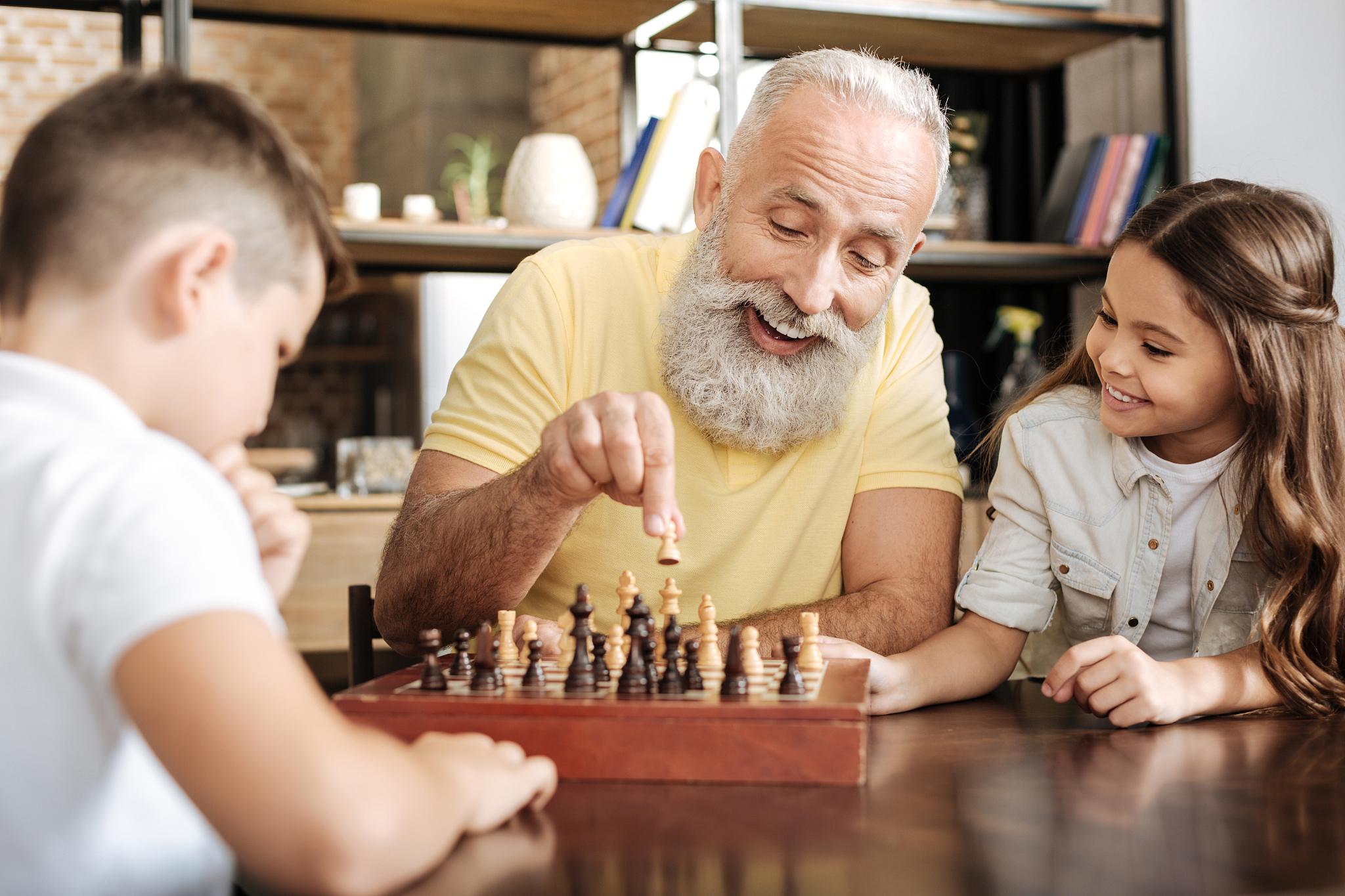 little girl watching her brother and grandfather play chess