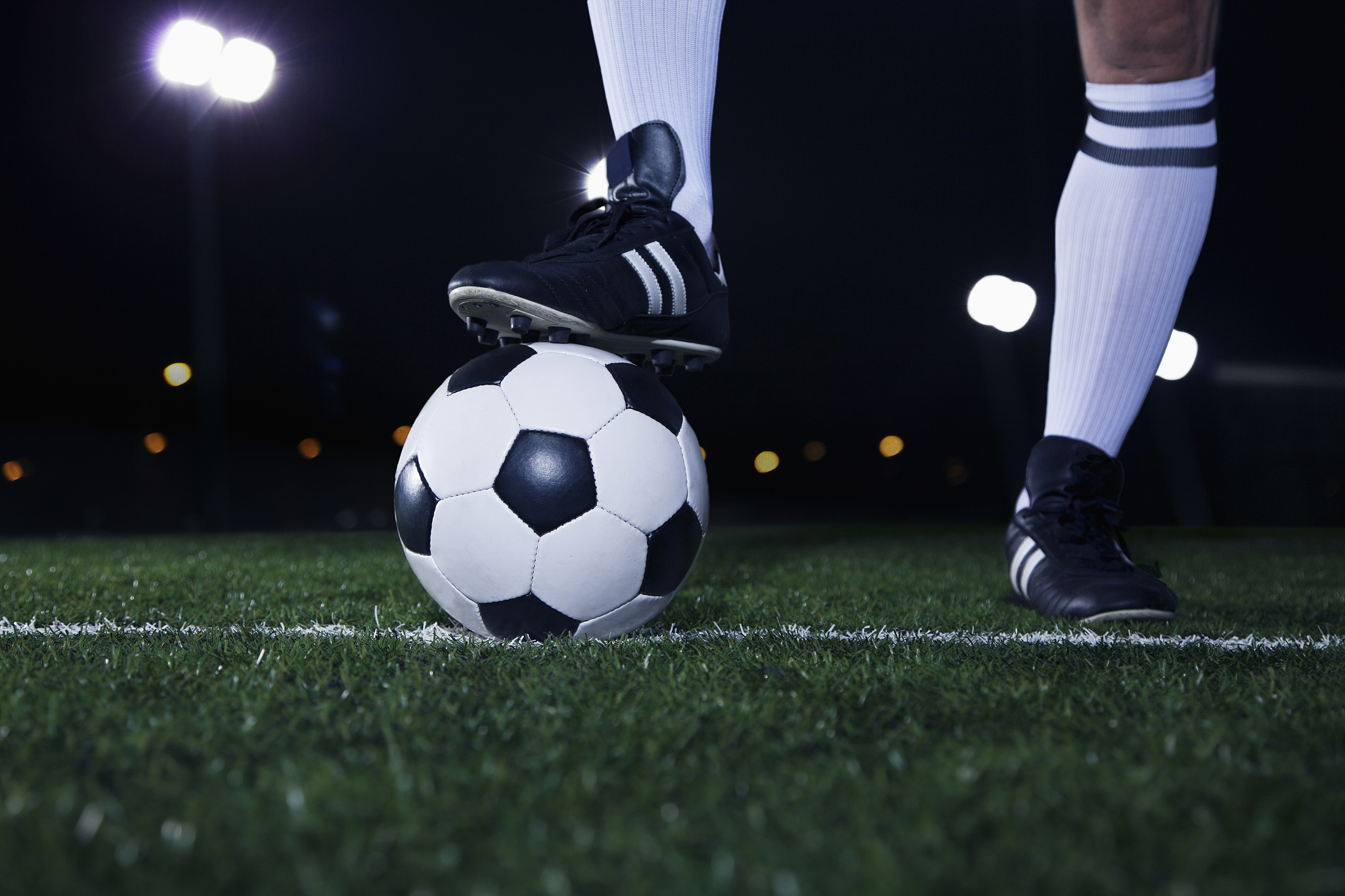 close up of feet on top of soccer ball on the line, night time i