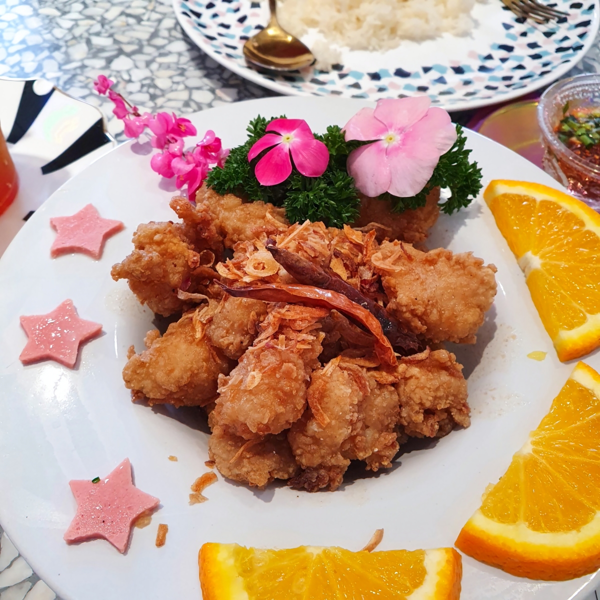 泰式香脆金黄炸鸡,饰以新鲜橙片和粉色花朵,盛装在性