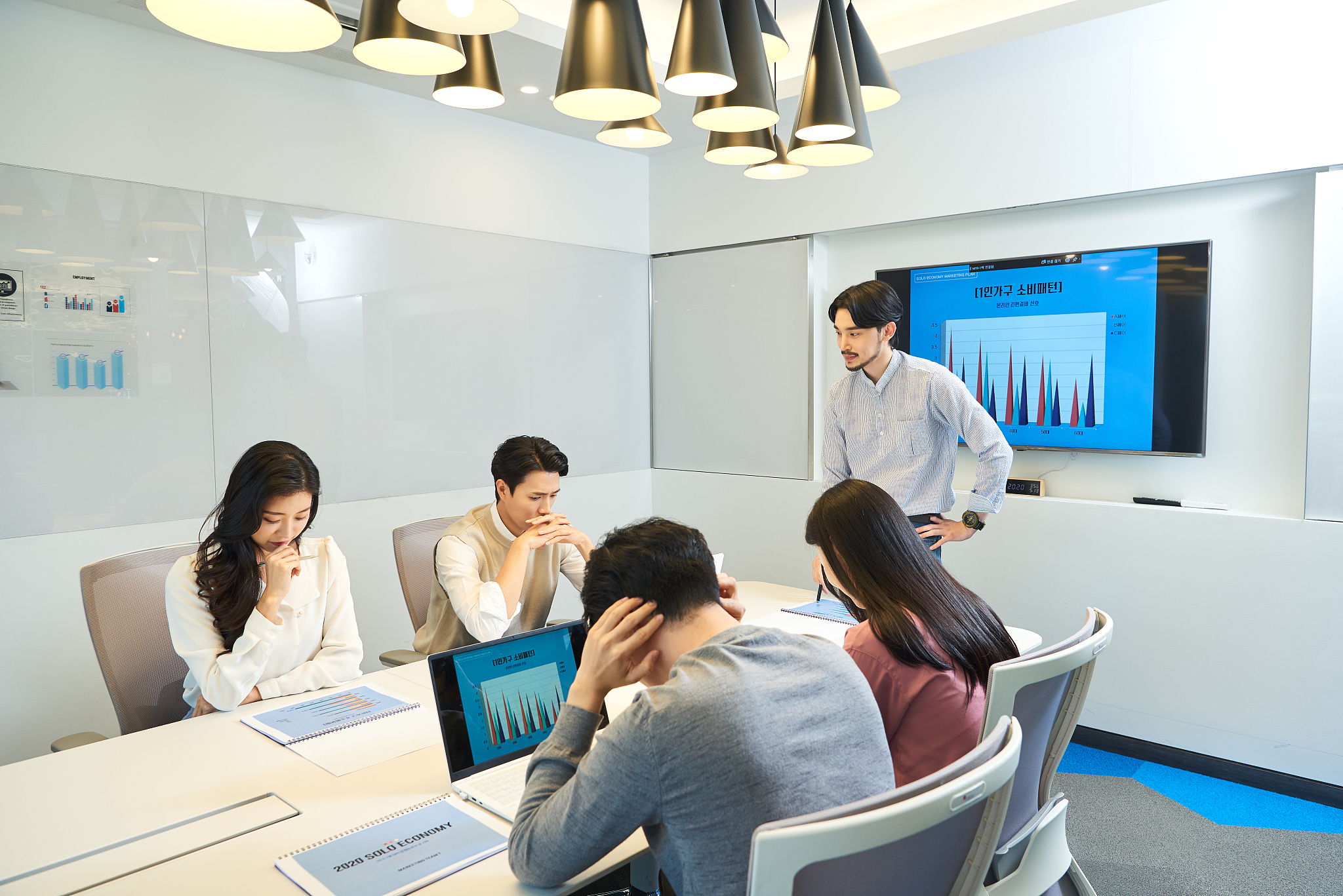 man standing by board discussing with coworkers looking at monit