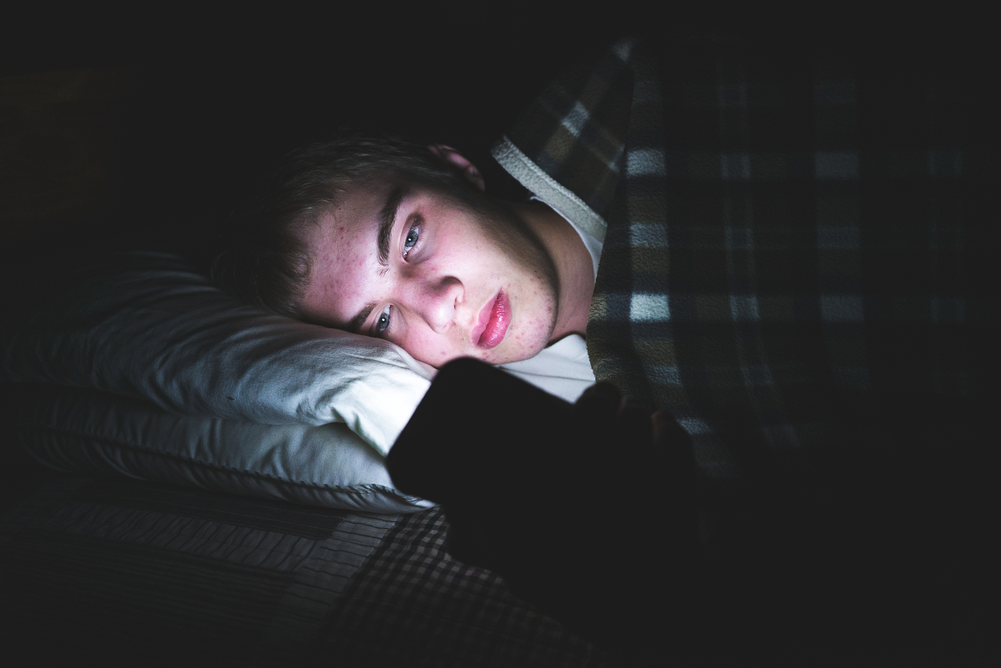 depressed teenager on his phone in the dark.