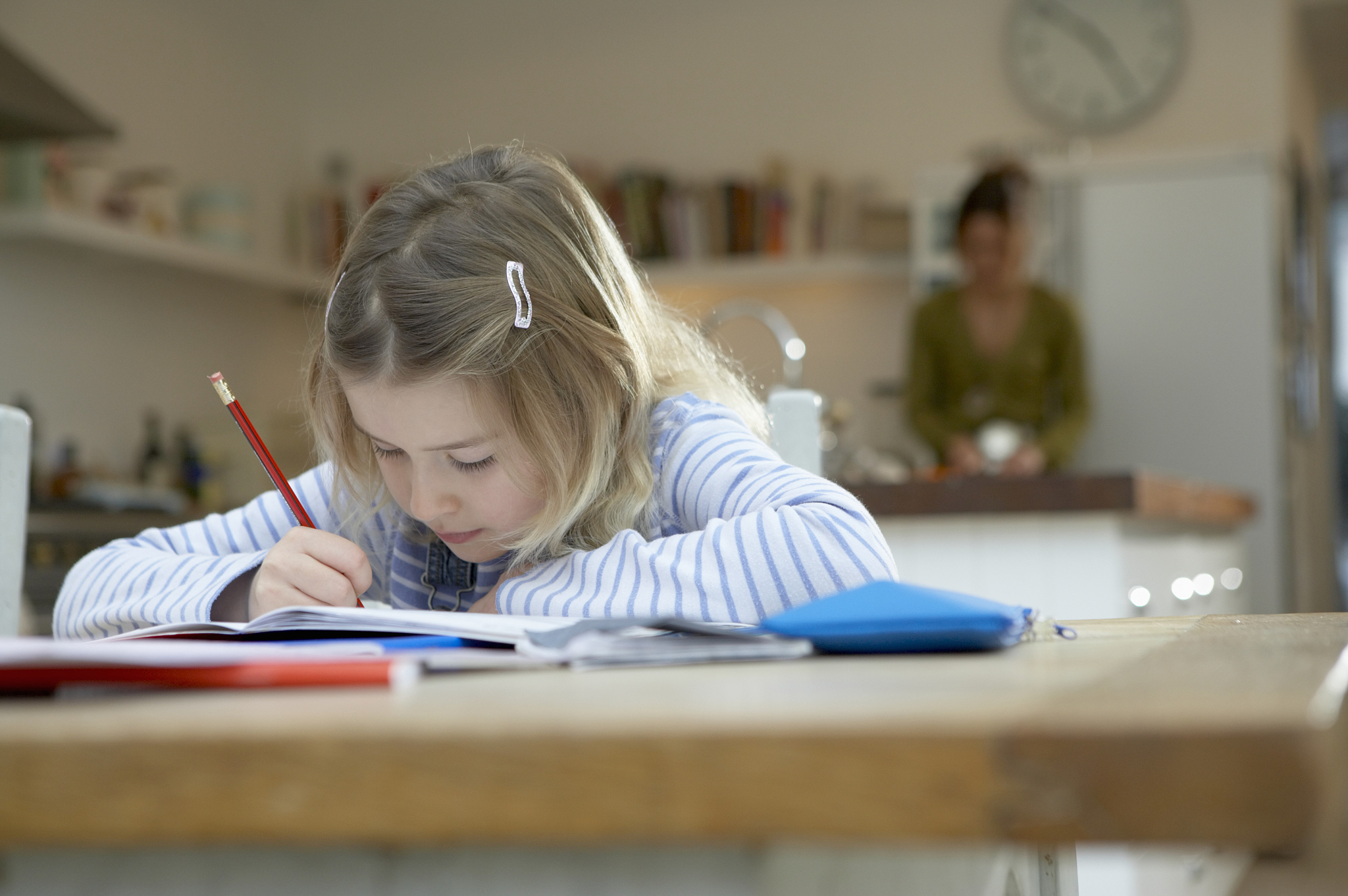 girl (6-8) writing in book at table by kitchen