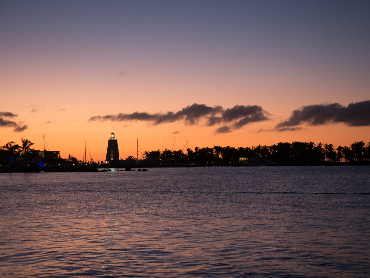 用文艺一点的文字表述一张在深圳湾公园拍摄的照片：在一排高低不齐的高楼大厦中太阳落下只剩下一点余光洒在海面上波光粼粼