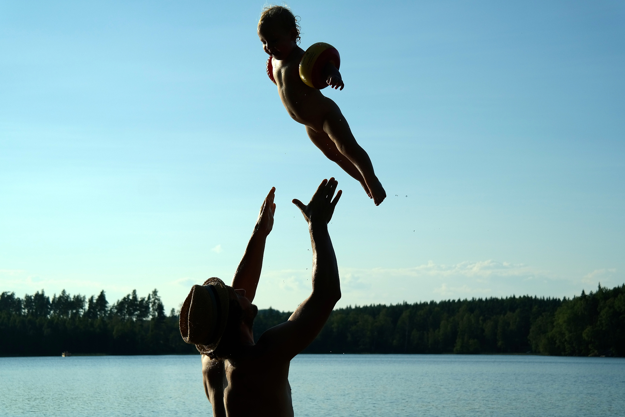 man throwing girl while playing in lake against sky