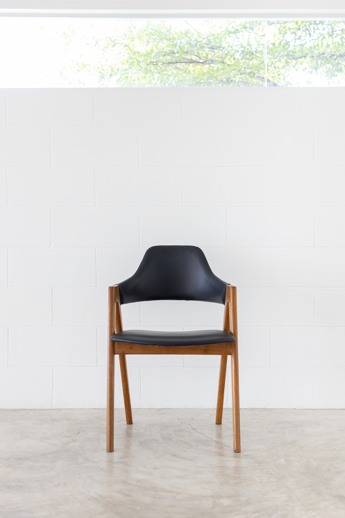 front view of single wooden leather chair on white concrete wall