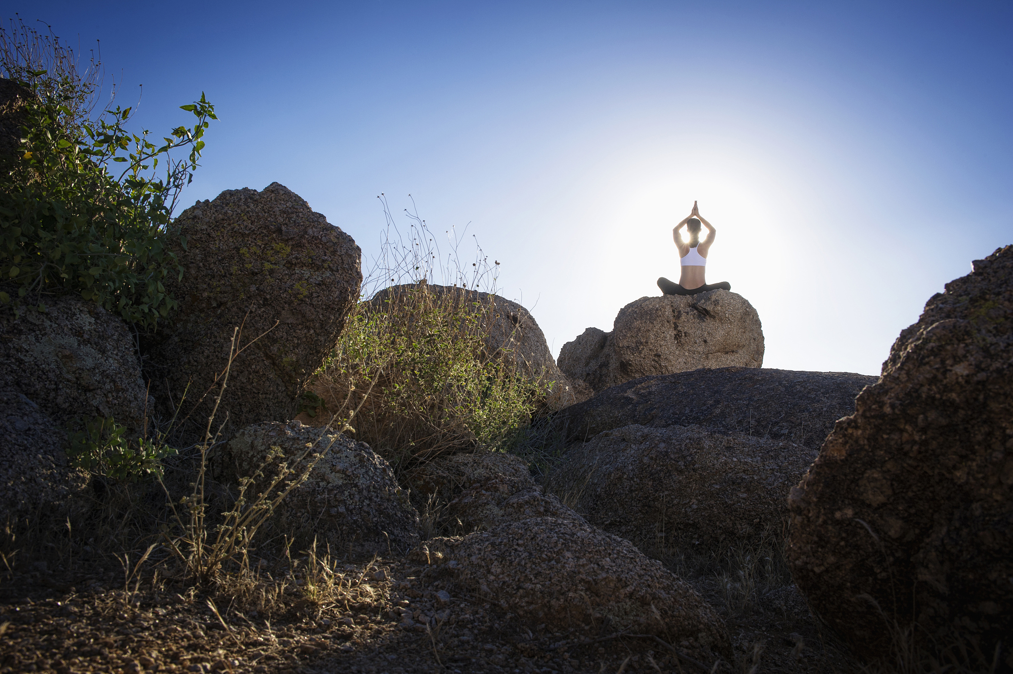 caucasian woman practicing yoga on rock formation under sunny sk