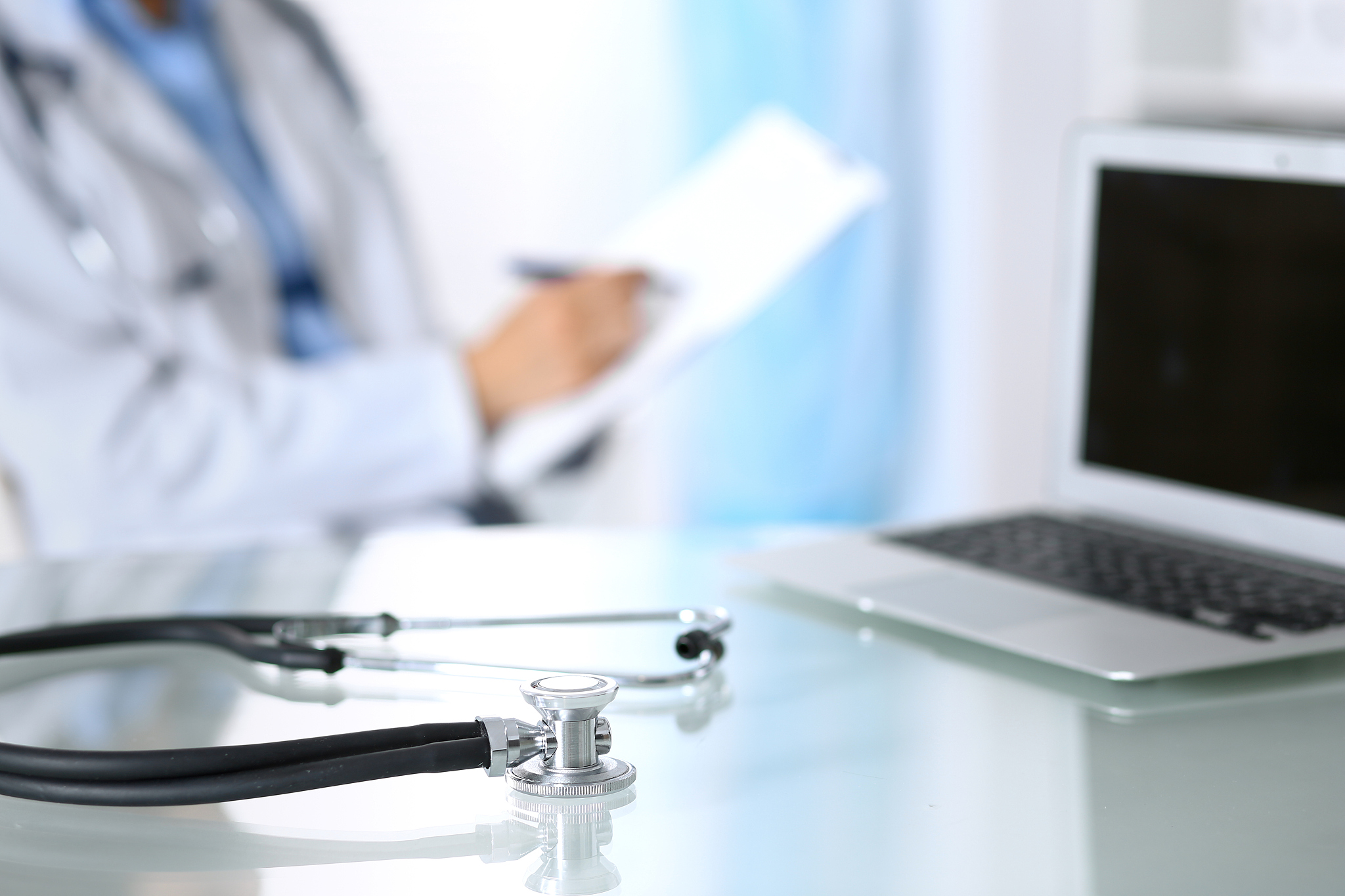 stethoscope lying on glass desk with laptop computer at busy phy