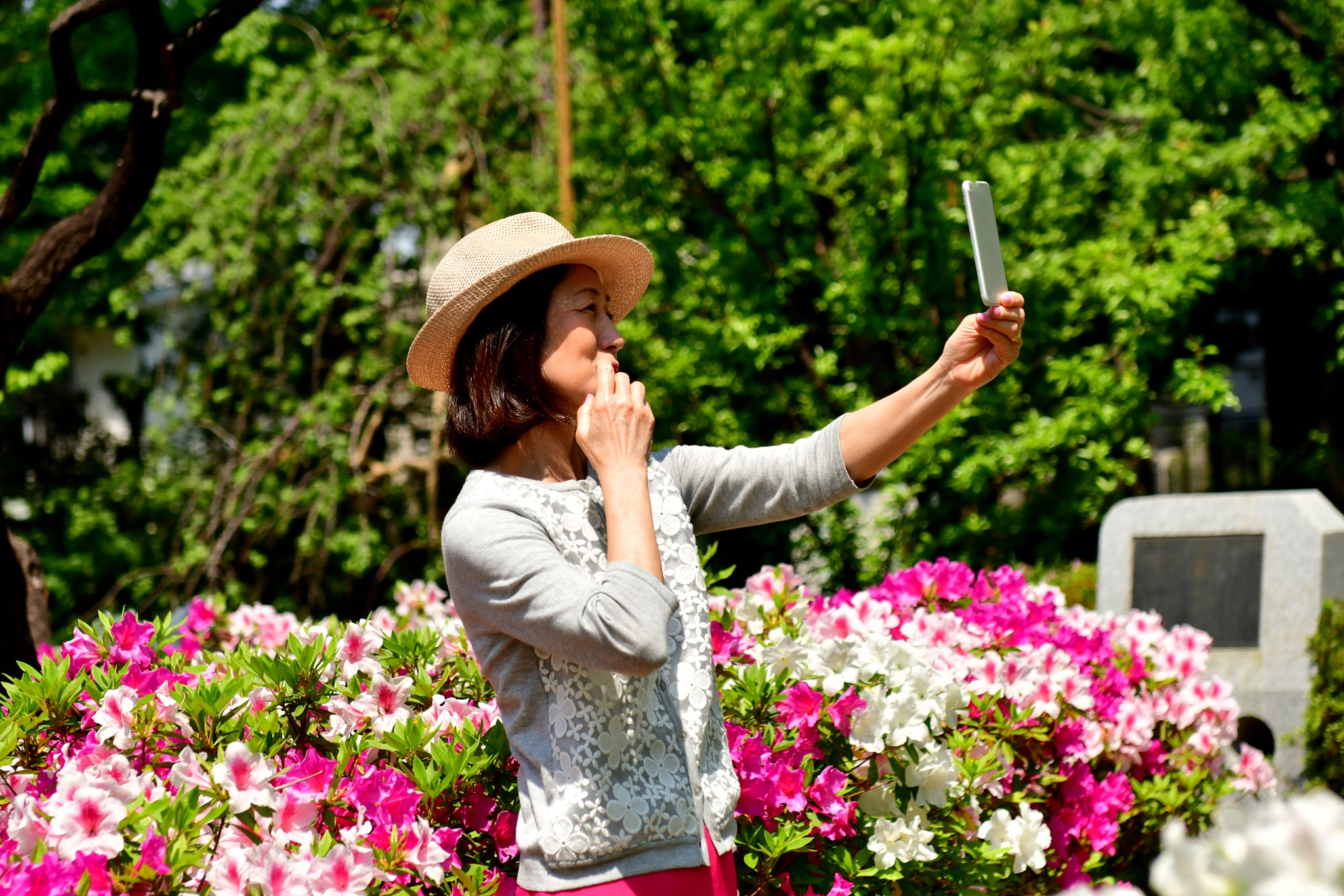 japanese woman taking selfie in park with azalea in full bloom
