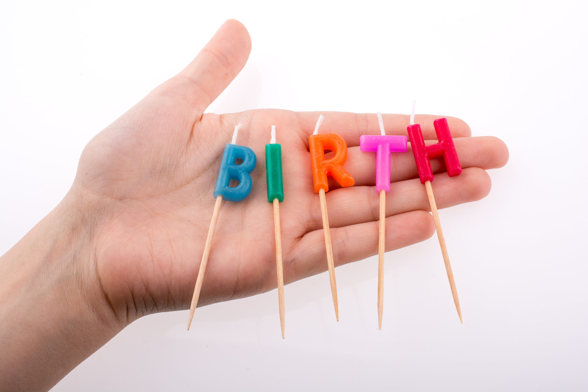 close-up of hand holding multi colored candle against white back
