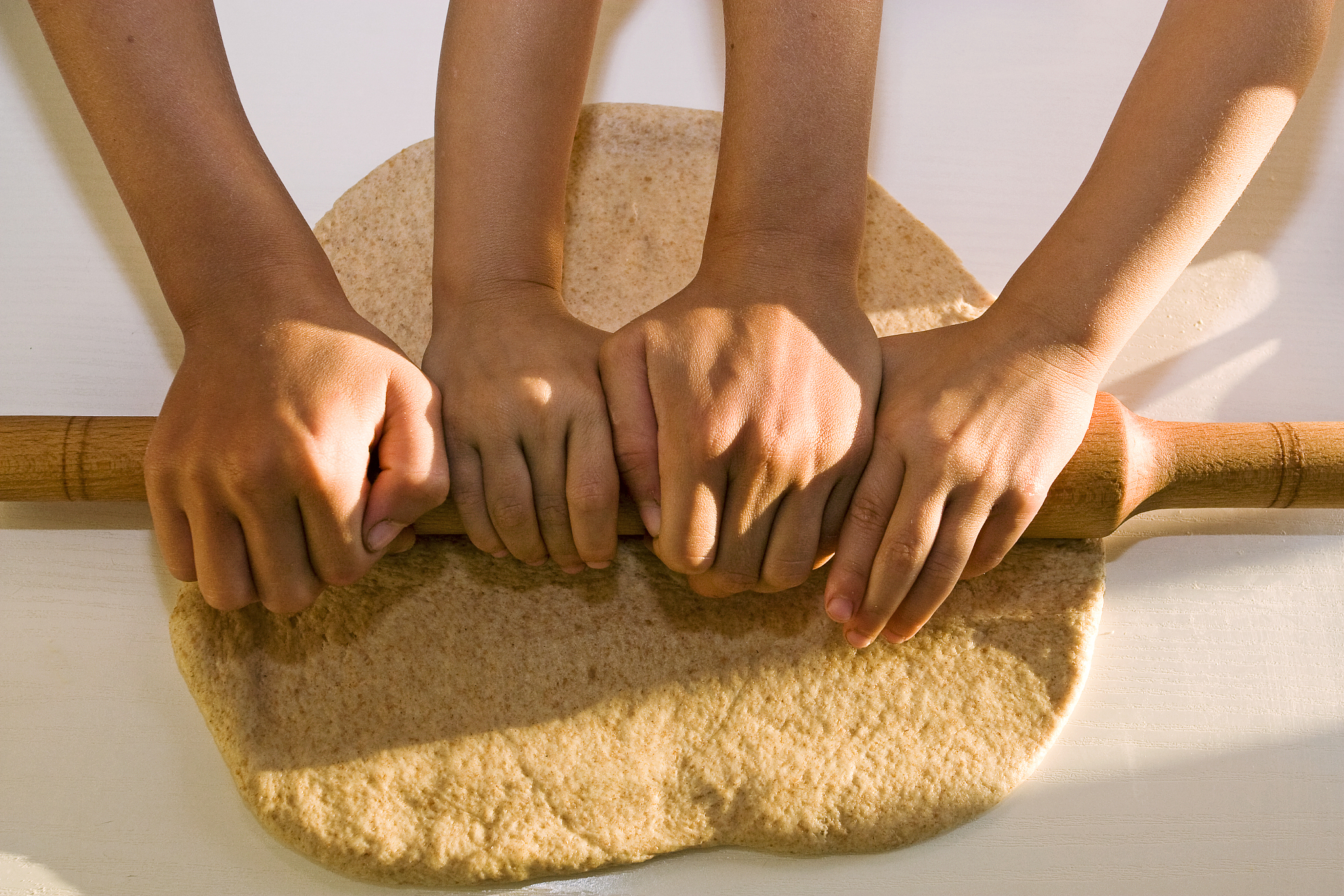 four hands roll out the dough