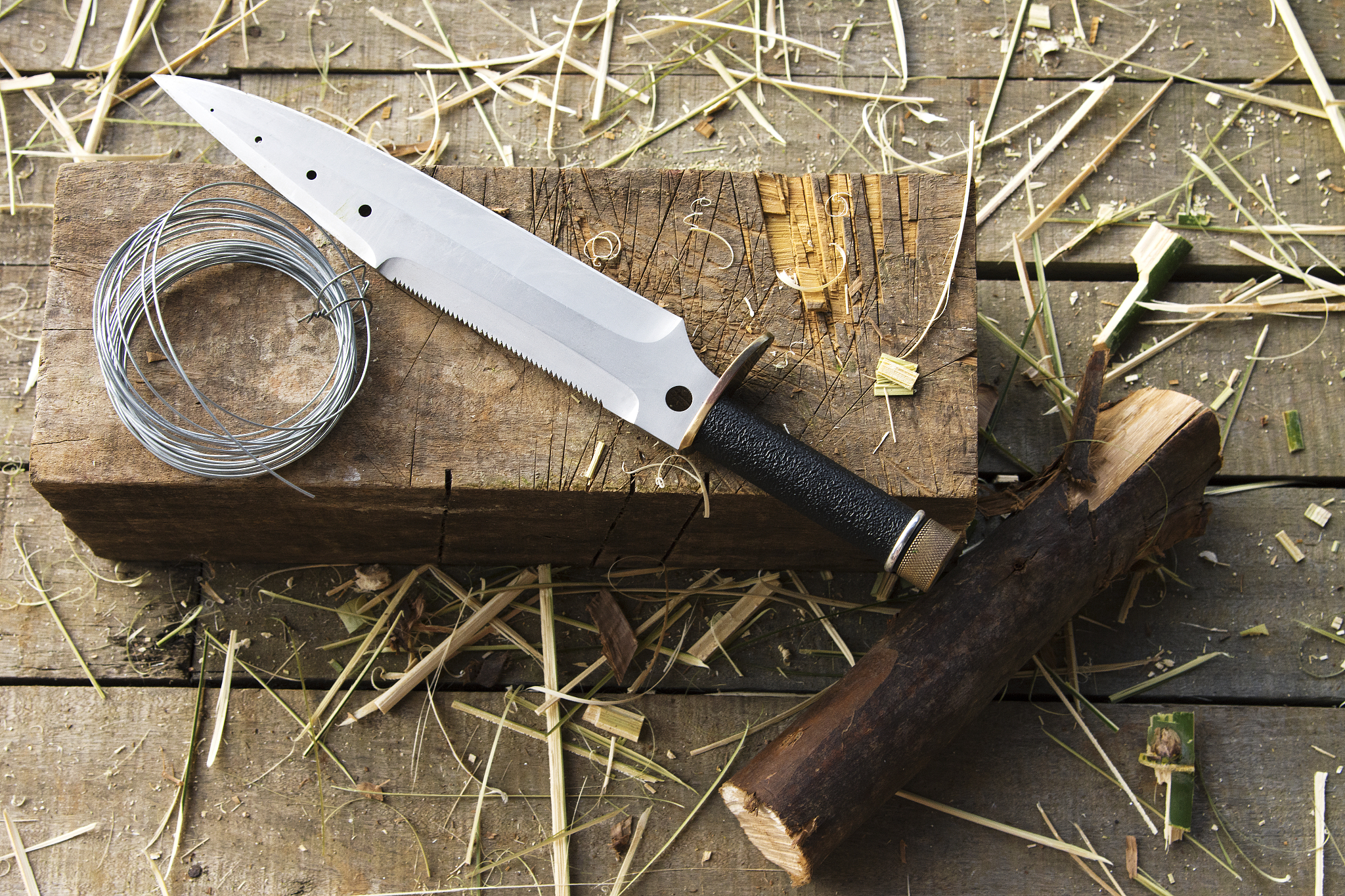 a survival knife with a wire roll over a wood block. still life.