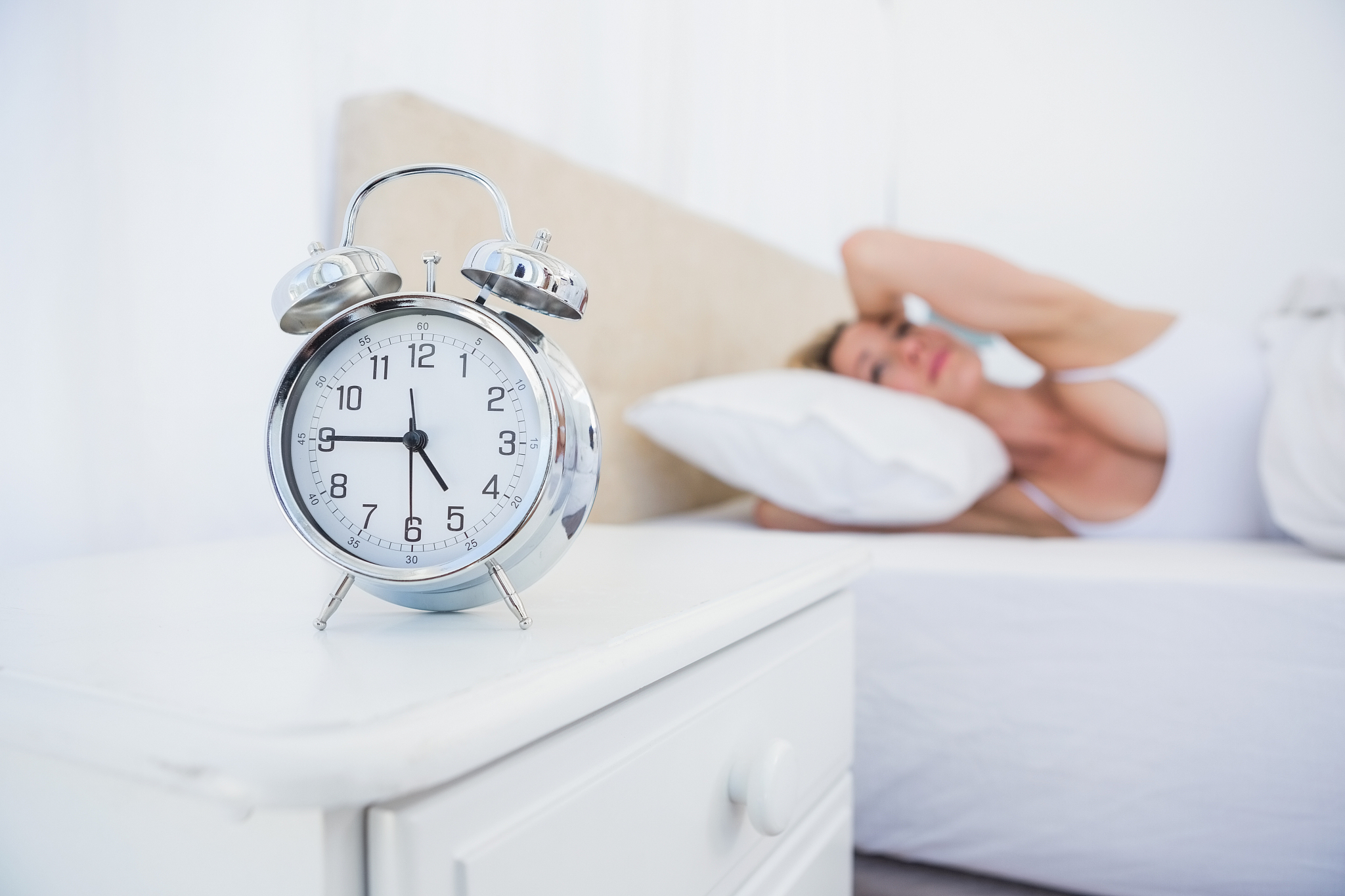 annoyed woman covering her ears from alarm clock