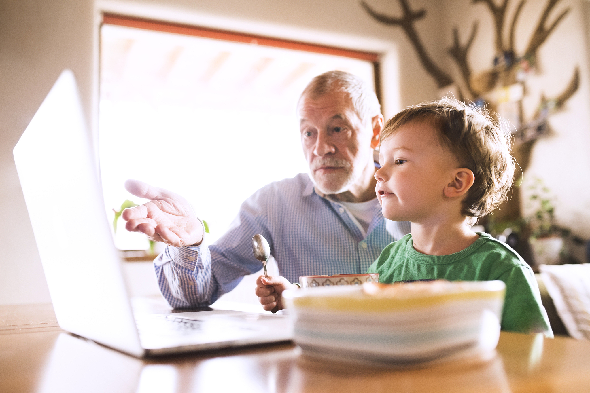 grandfather and grandson sitting at table, eating and using lapt