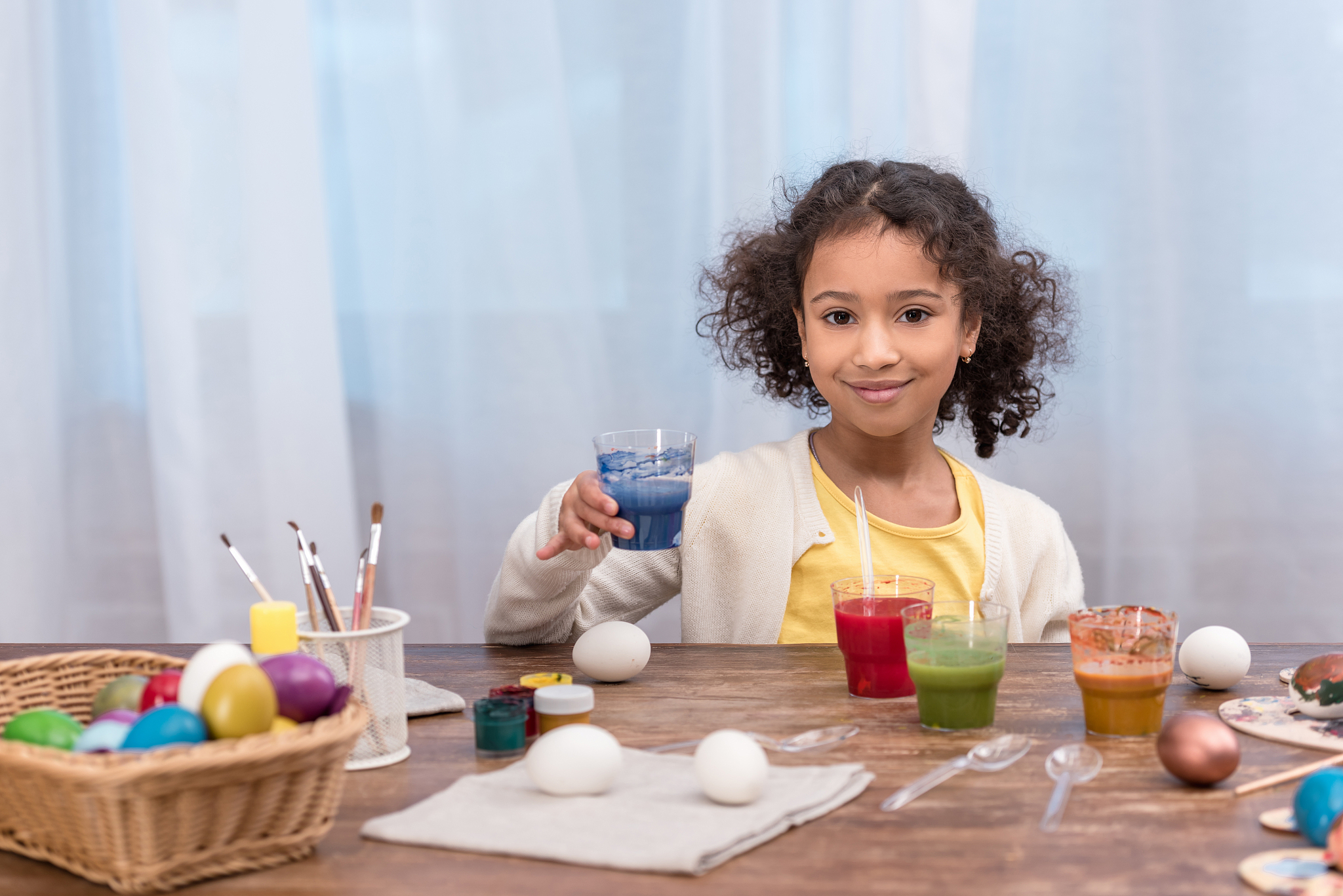 african american kid holding glass with paint for easter eggs an