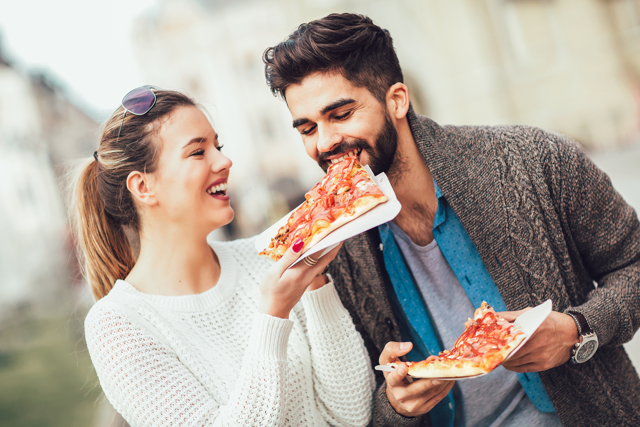 couple eating pizza outdoors and smiling.