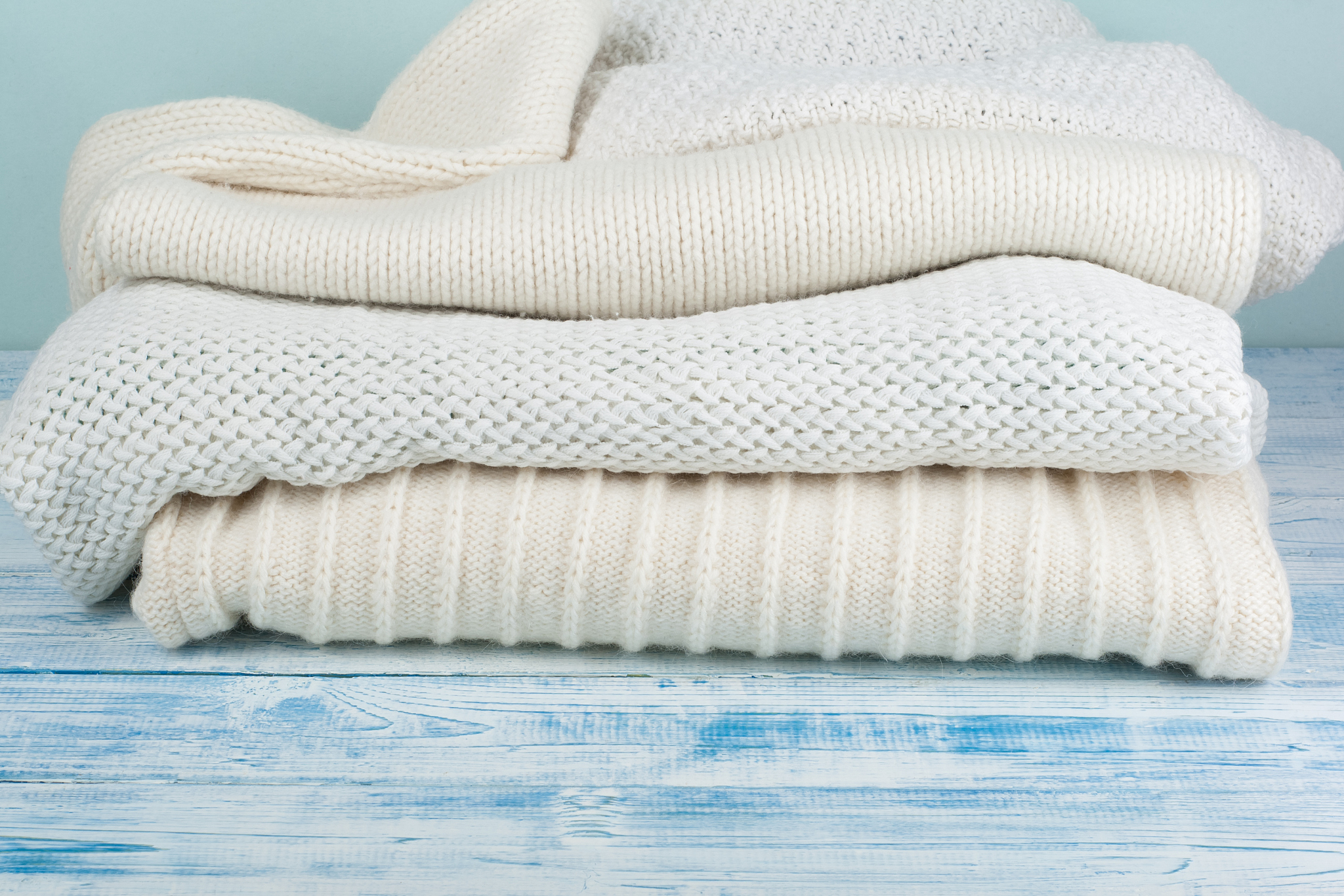 knitted wool sweaters. pile of knitted winter clothes on blue wo