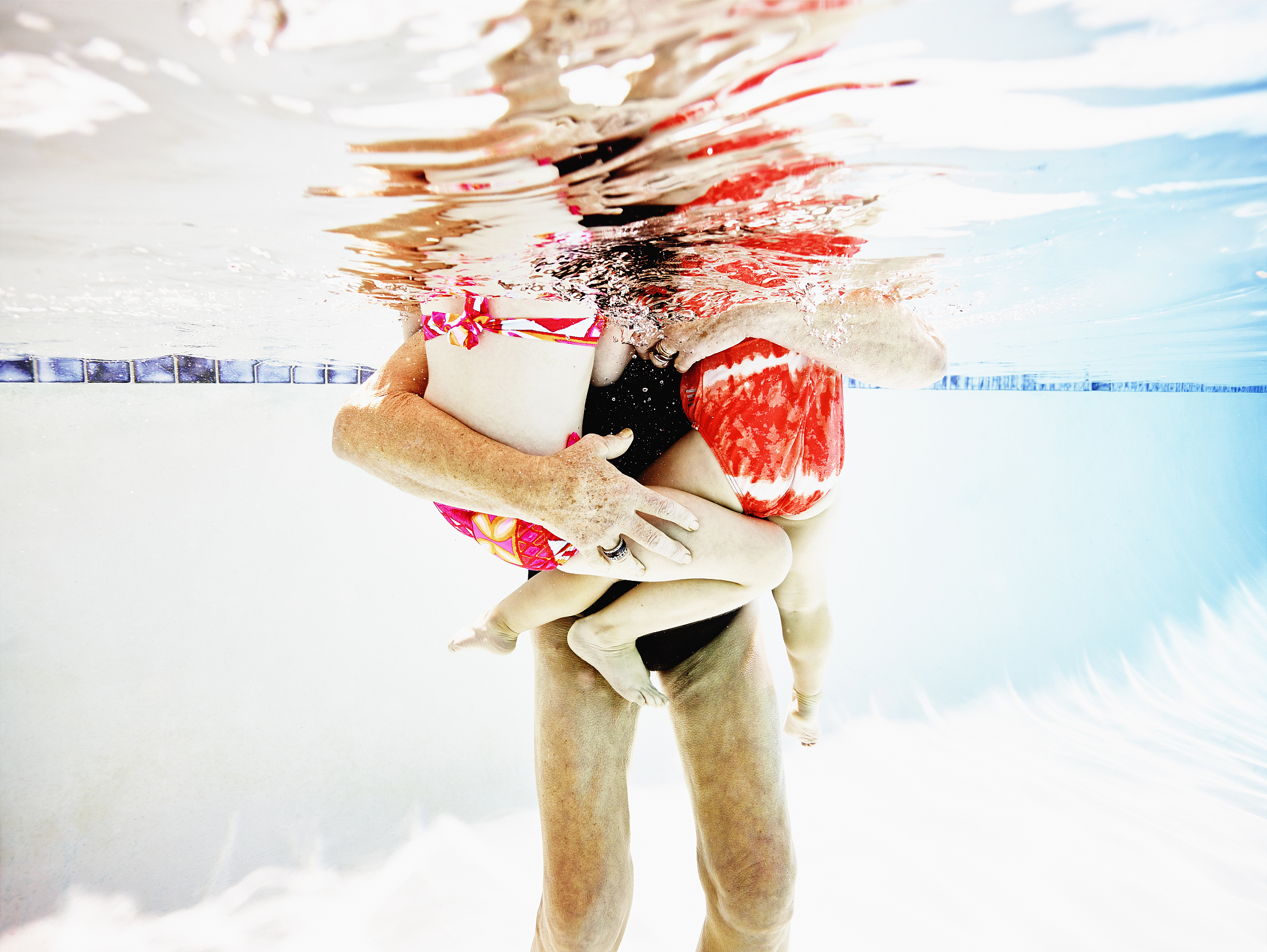 senior woman holding granddaughters in pool