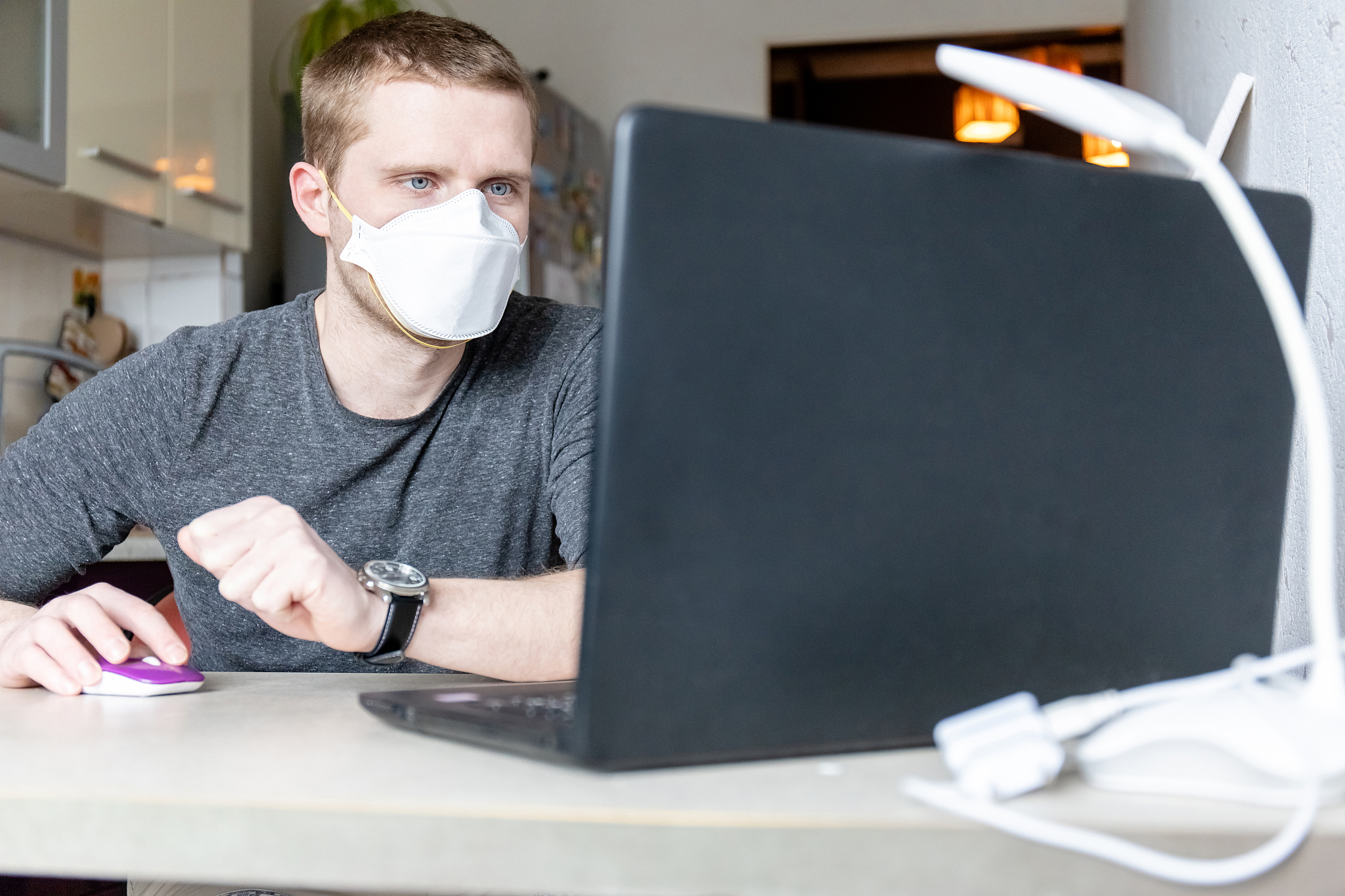 young man in protective medical mask works at a laptop at home, 