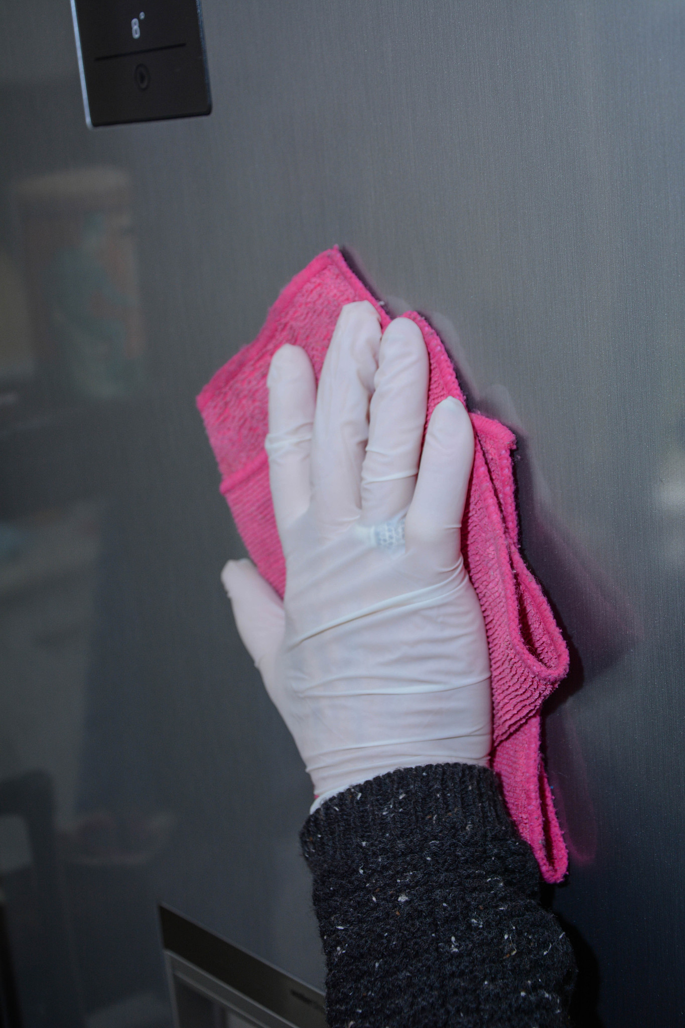 senior woman cleaning refrigerator door with a disinfection spra