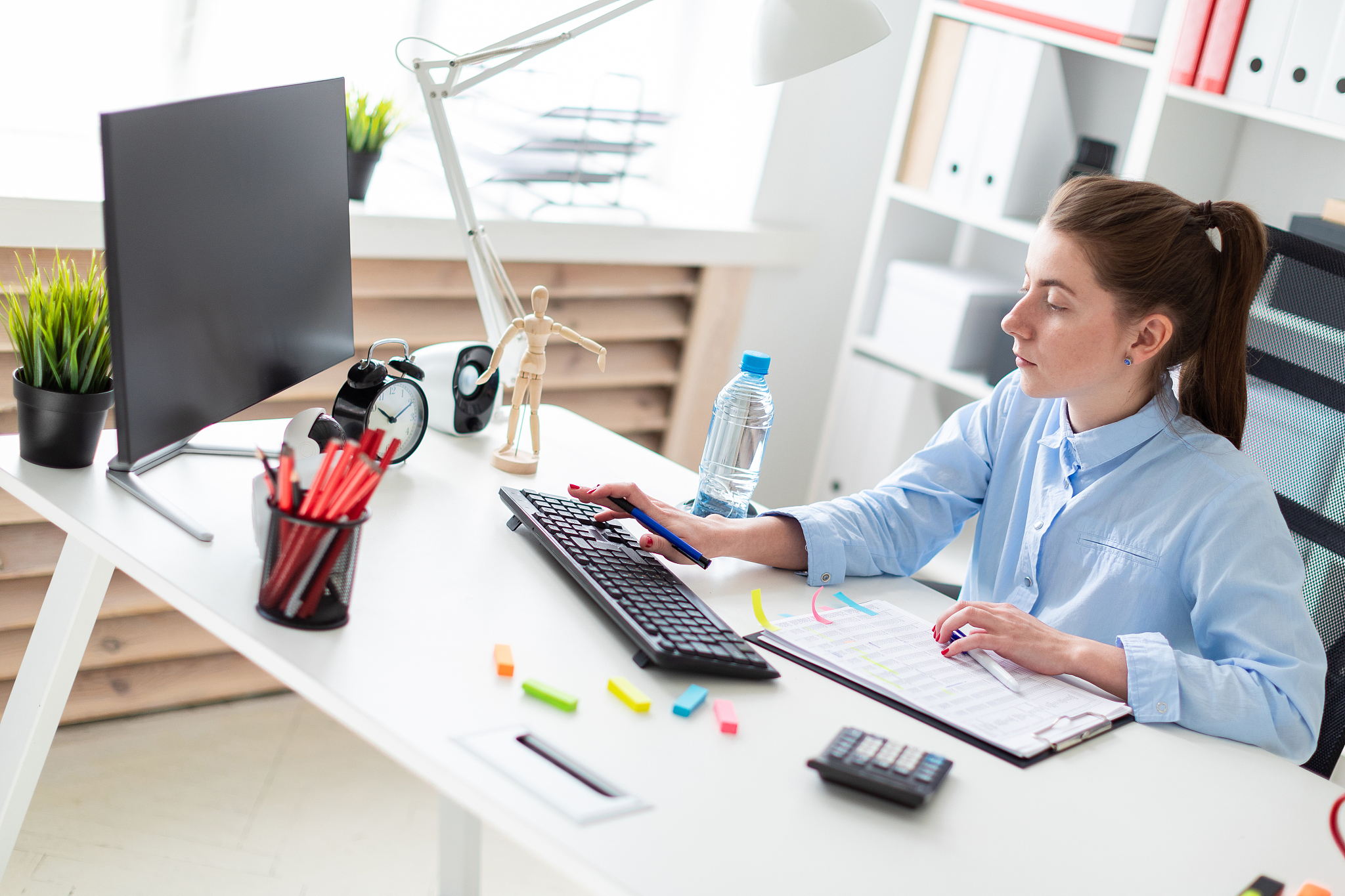 a young girl in the office sits at a table, holds a pen in her h