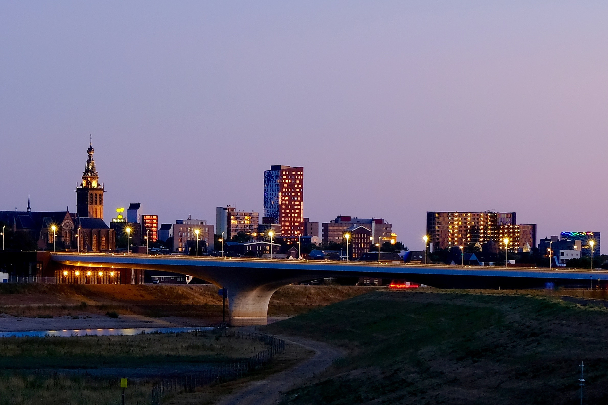 illuminated buildings by river against clear sky at night