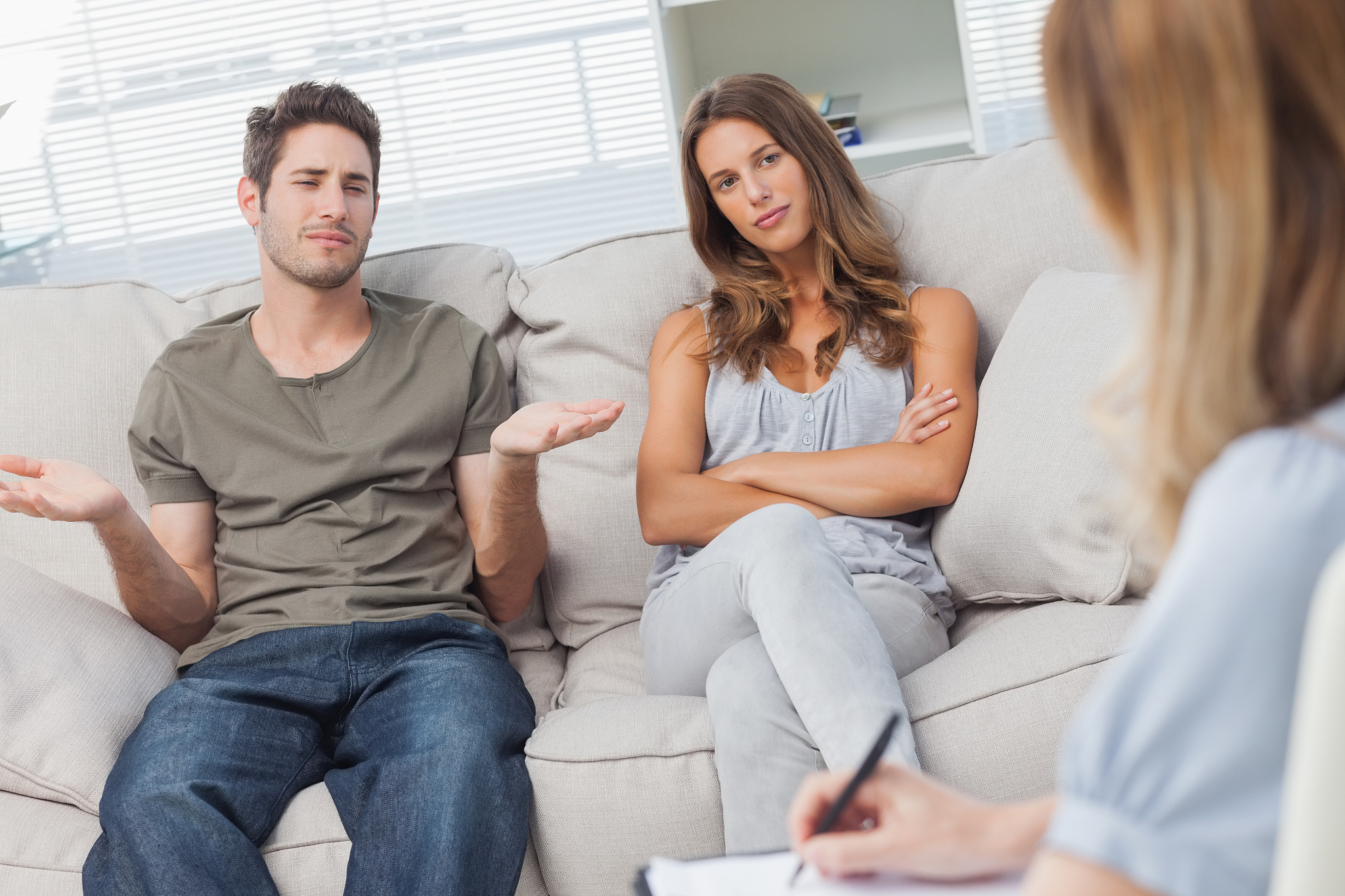 upset couple sit on a sofa with arms crossed
