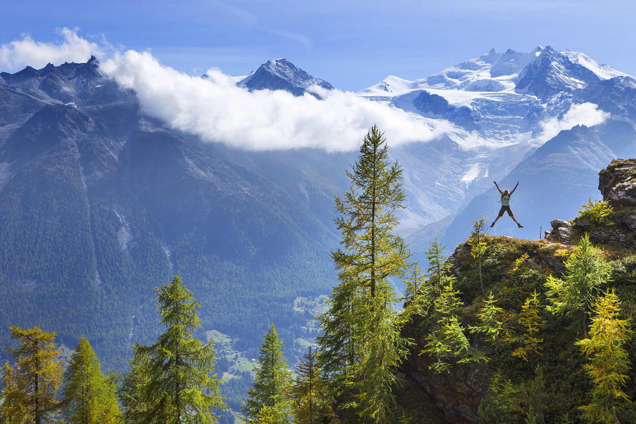 a female hiker is jumping in the air near embd, in the swiss alp