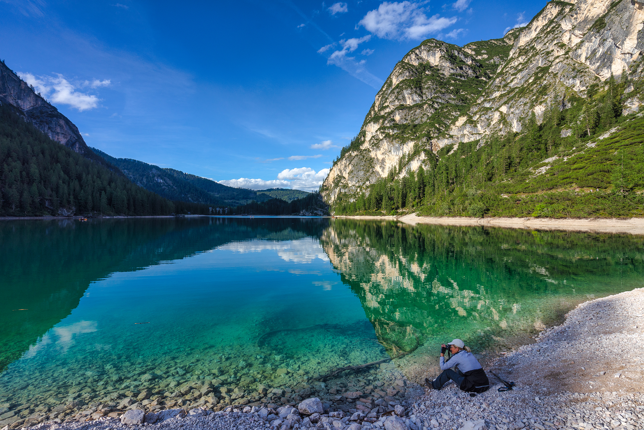 woman sitting by lake braies taking a photo, south tyrol, italy
