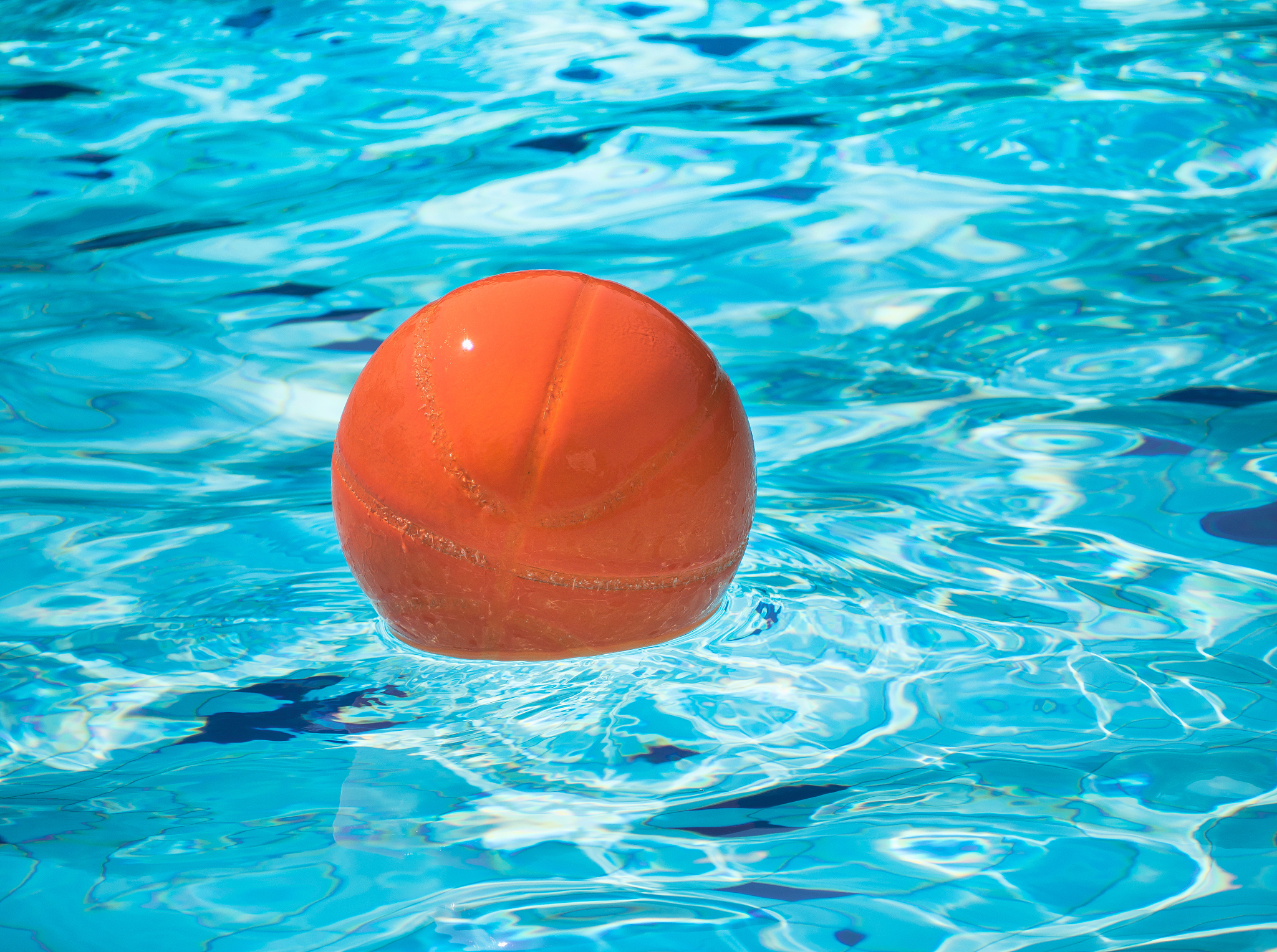 orange beach ball floating in blue swimming pool.