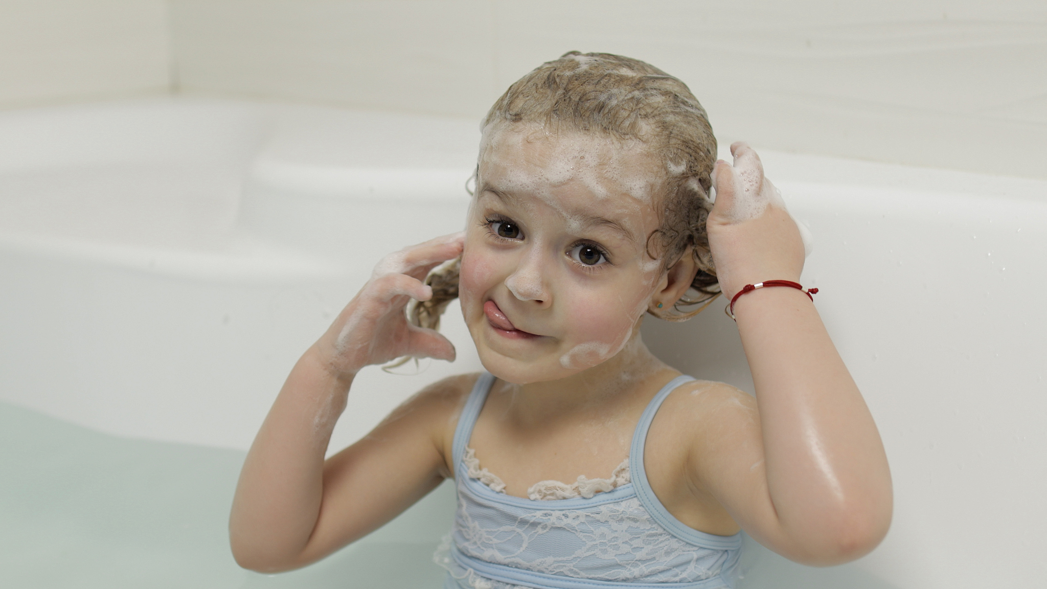 cute blonde girl takes a bath in swimwear. little child washes h