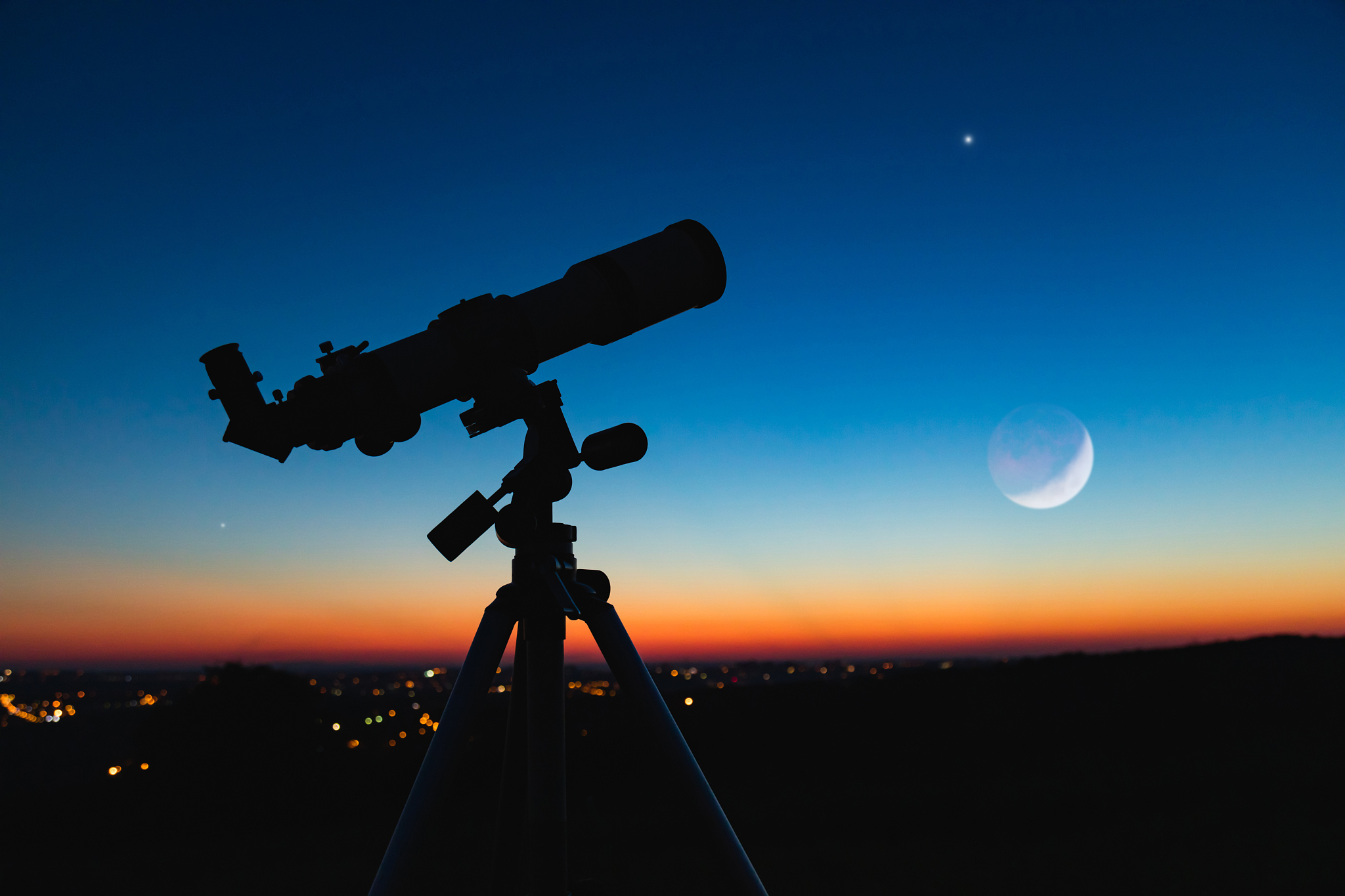 telescope silhouette and night sky with city lights in the backg