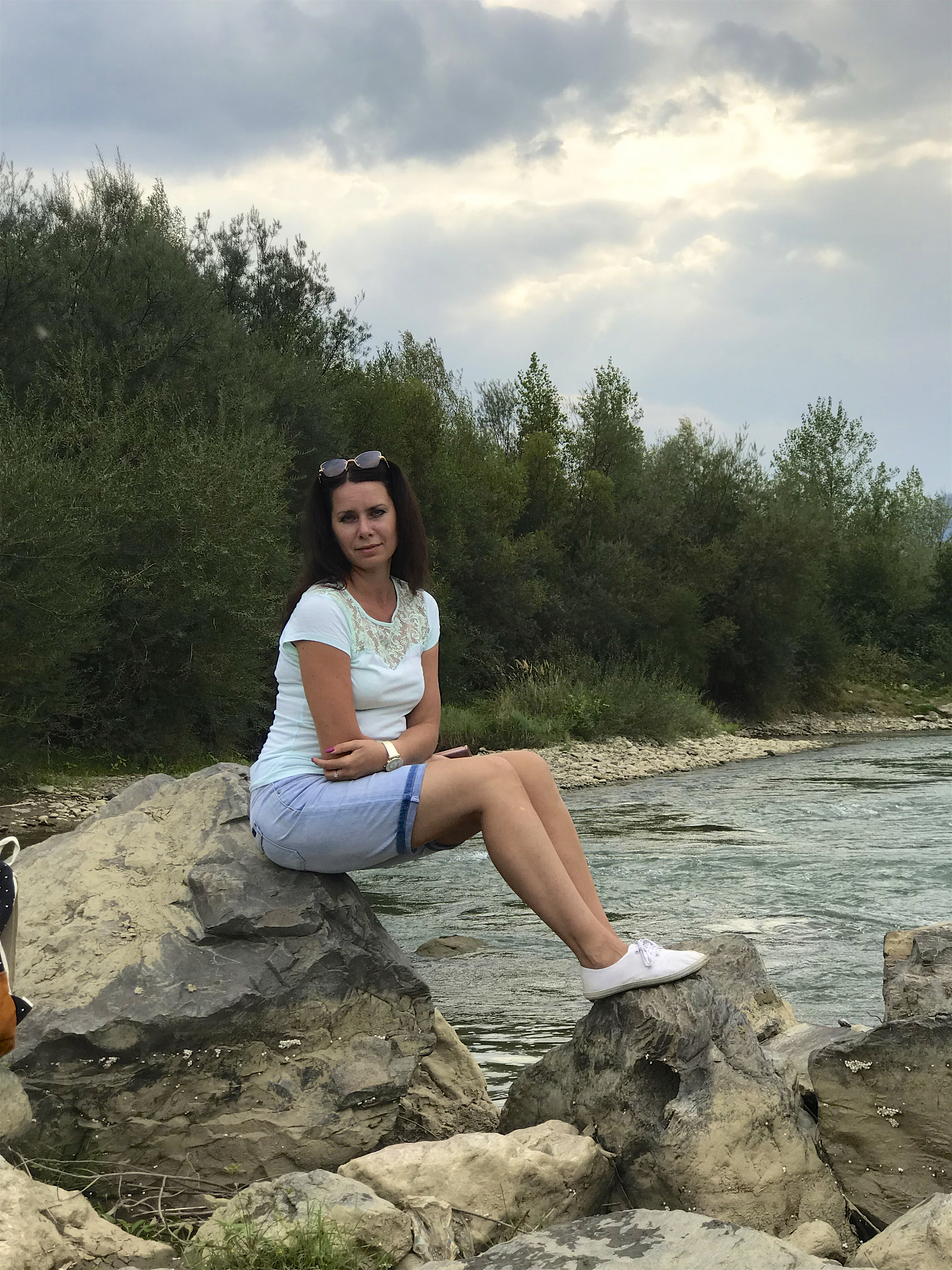 a girl sits on a large boulder near a mountain river. near a tou