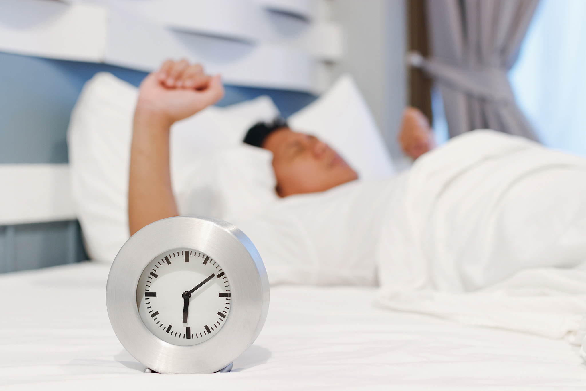 alarm clock waking up at morning with a man sleeping on bed.