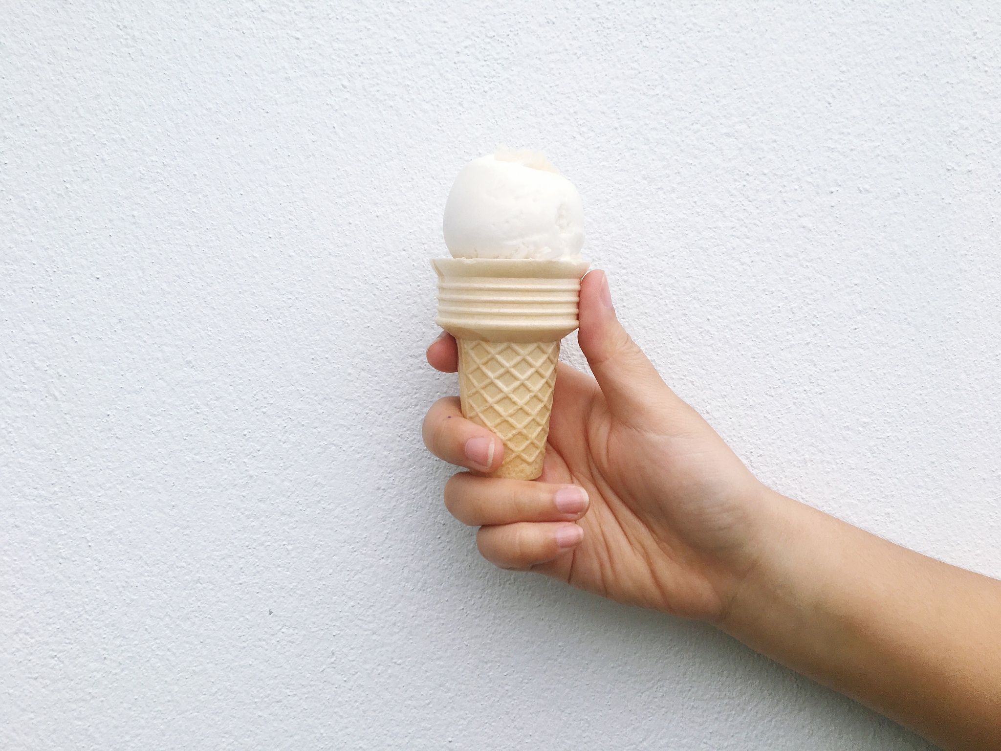 cropped hand holding ice cream against wall