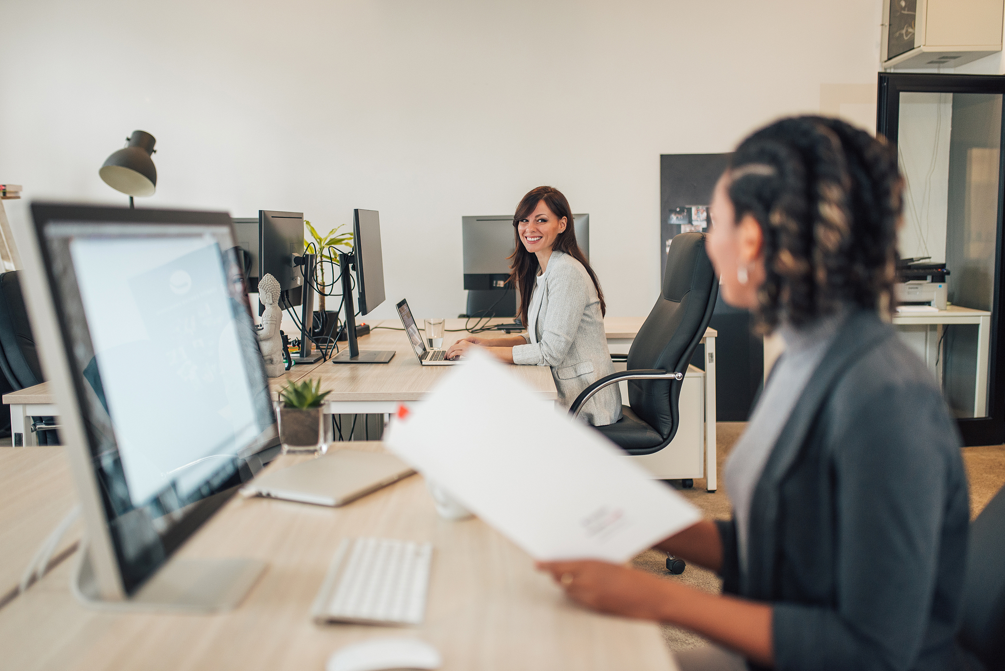 two smiling woman working and talking in co working office.