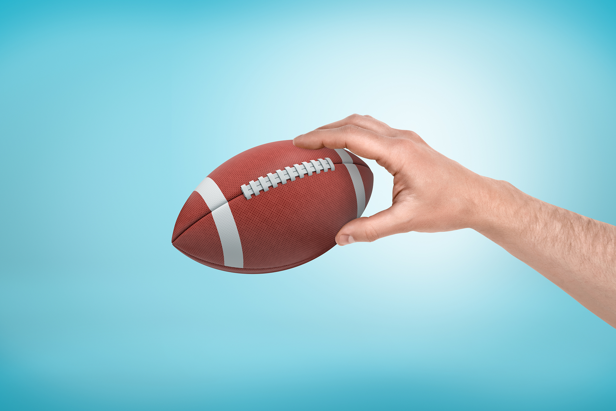 man's hand holding ball for american football on light blue grad