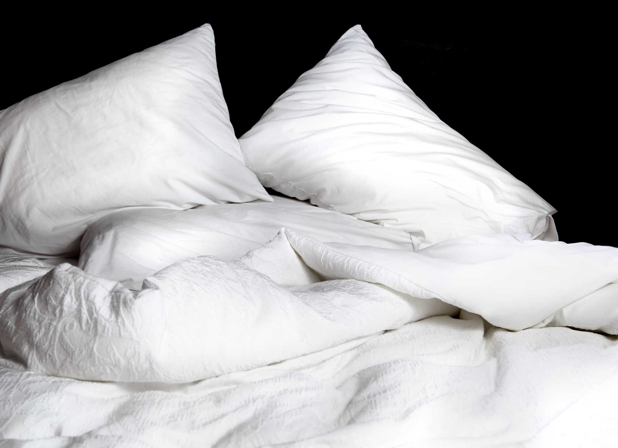 unmade bed of white linens pillows blanket