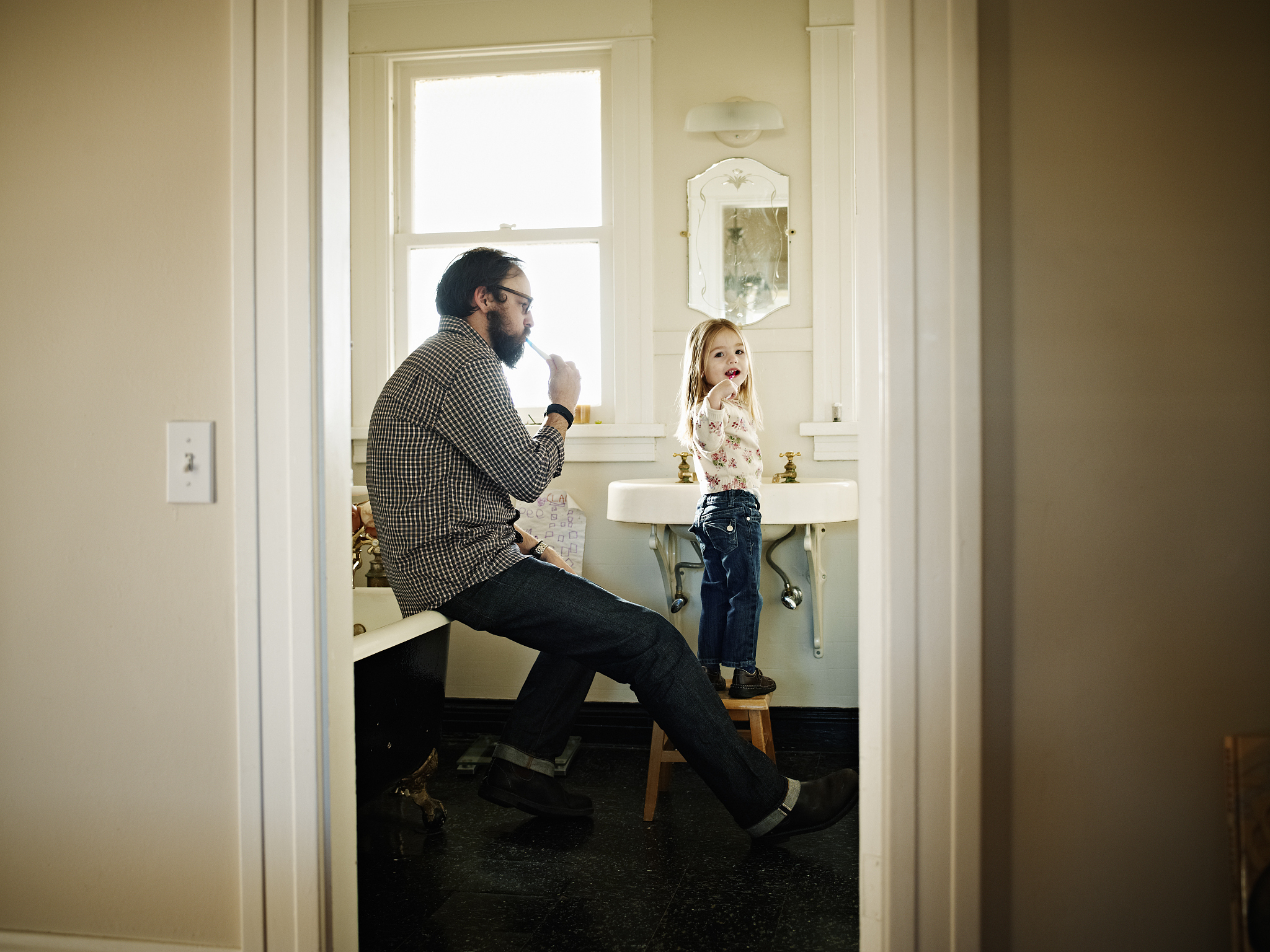 father and daughter brushing teeth in bathroom