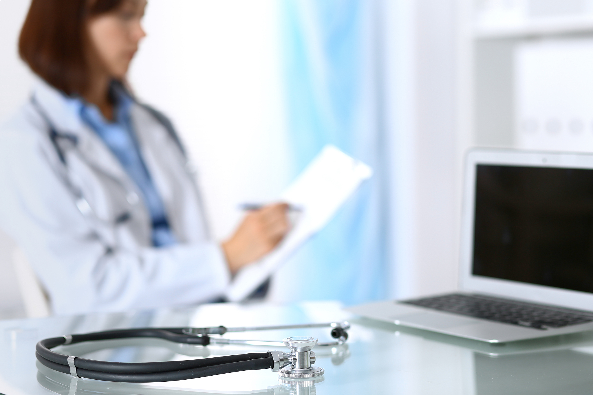 stethoscope lying on glass desk with laptop computer at busy phy